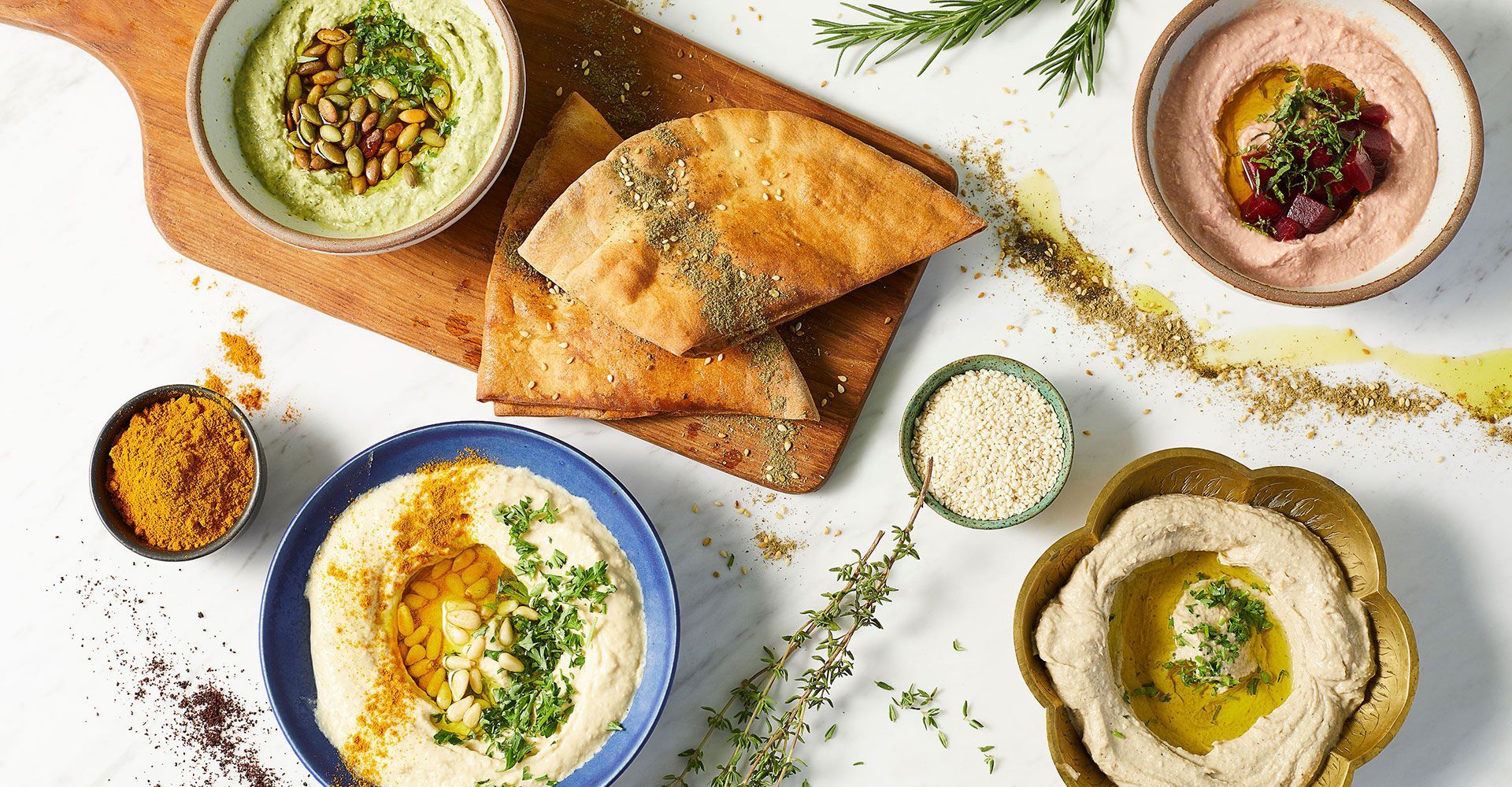 A table topped with bowls of hummus and pita bread.
