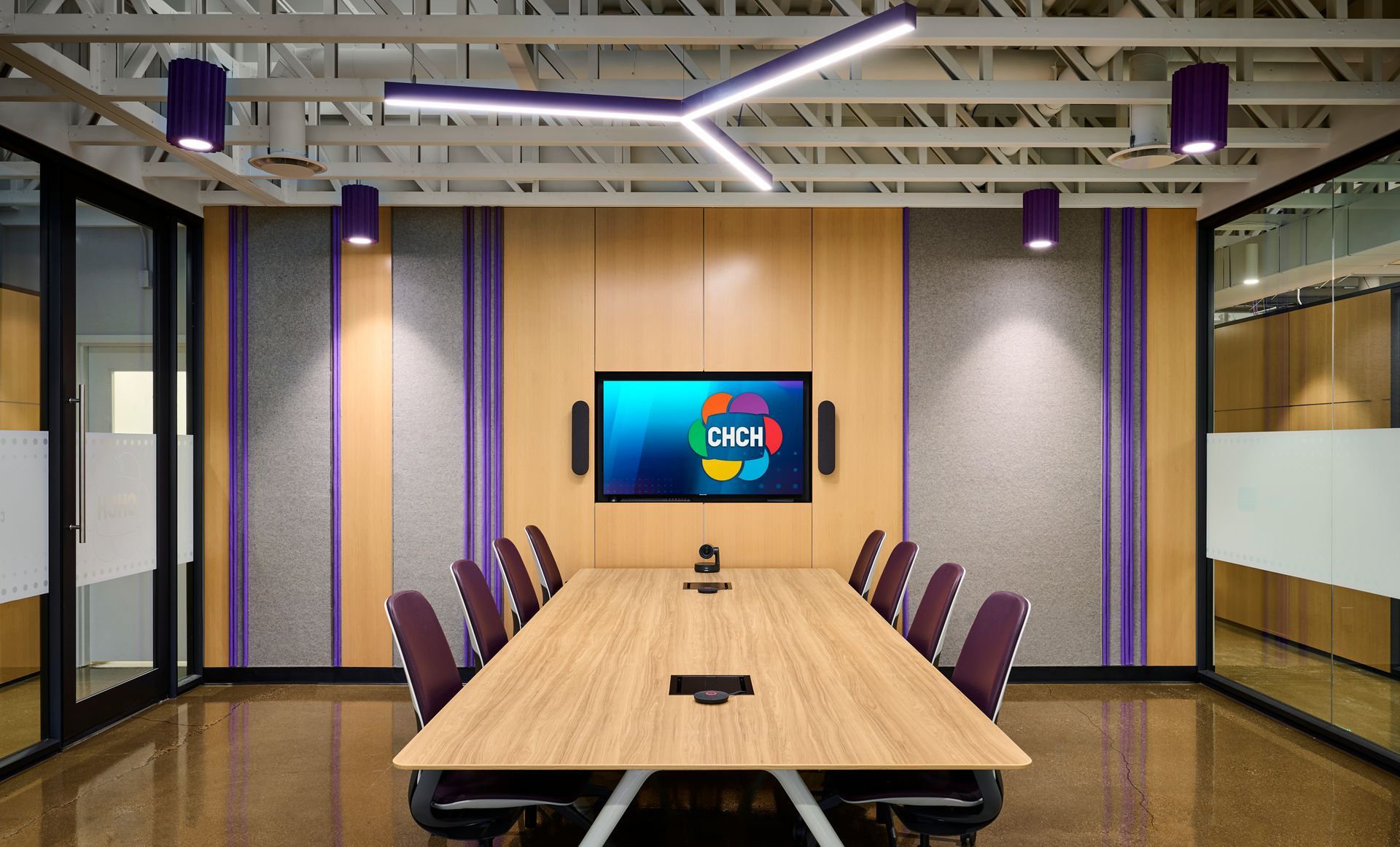 A conference room with a long wooden table and chairs and a flat screen tv on the wall.
