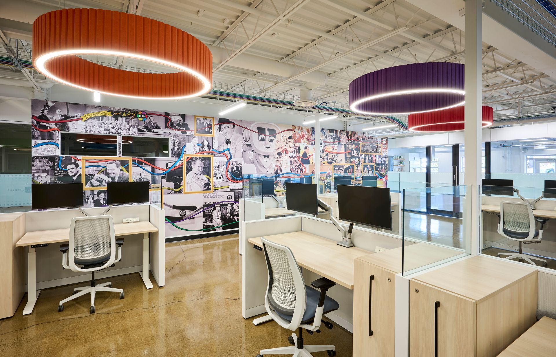 A large office with lots of desks and chairs and a mural on the wall.