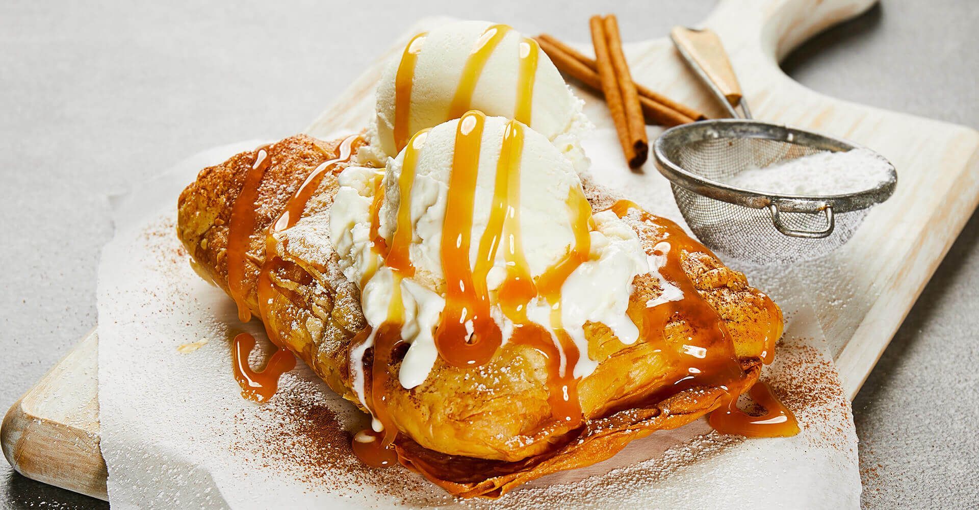 A close up of a dessert with ice cream and caramel sauce on a cutting board.