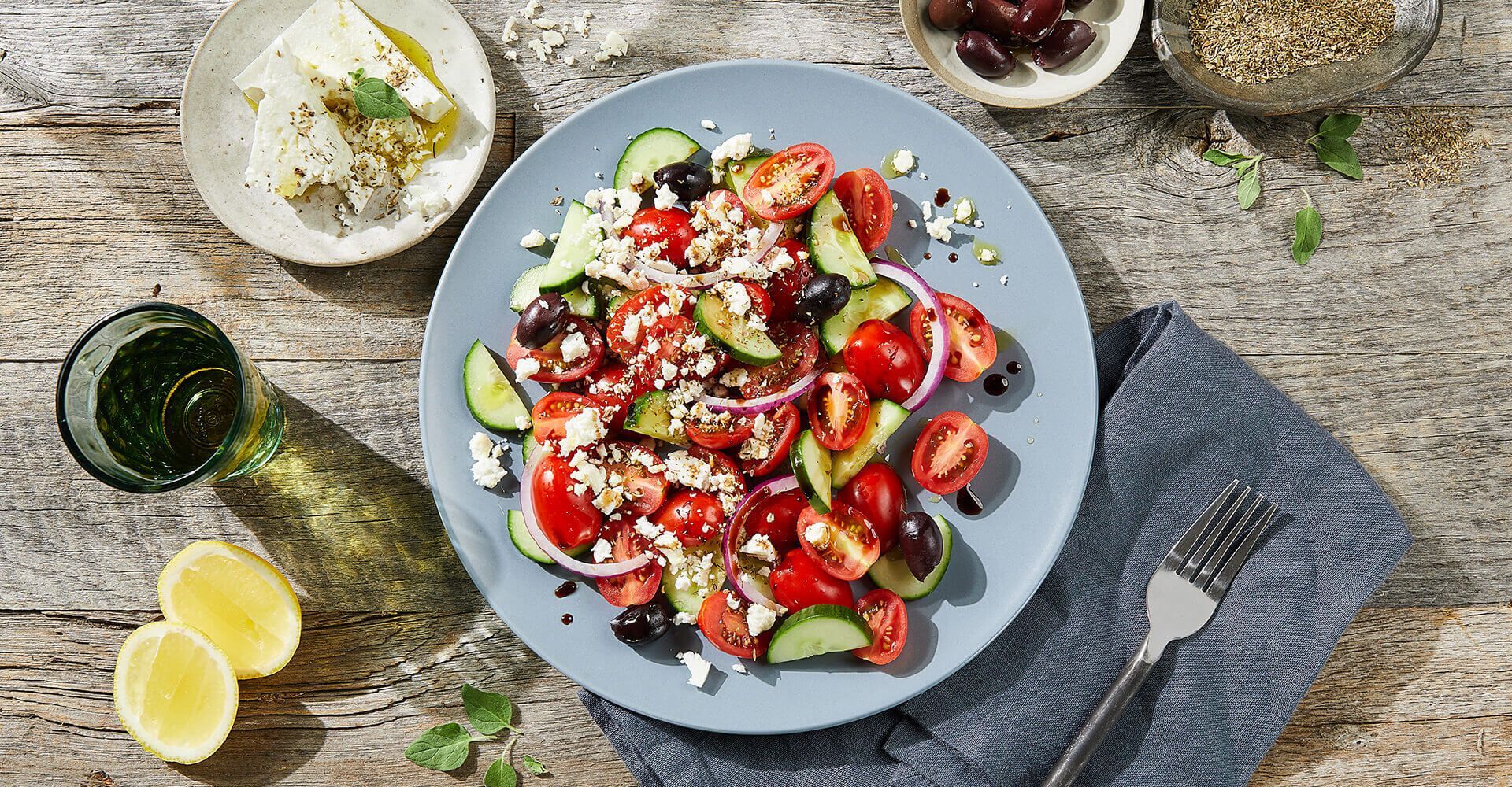 A plate of salad with tomatoes , cucumbers , olives and feta cheese on a wooden table.