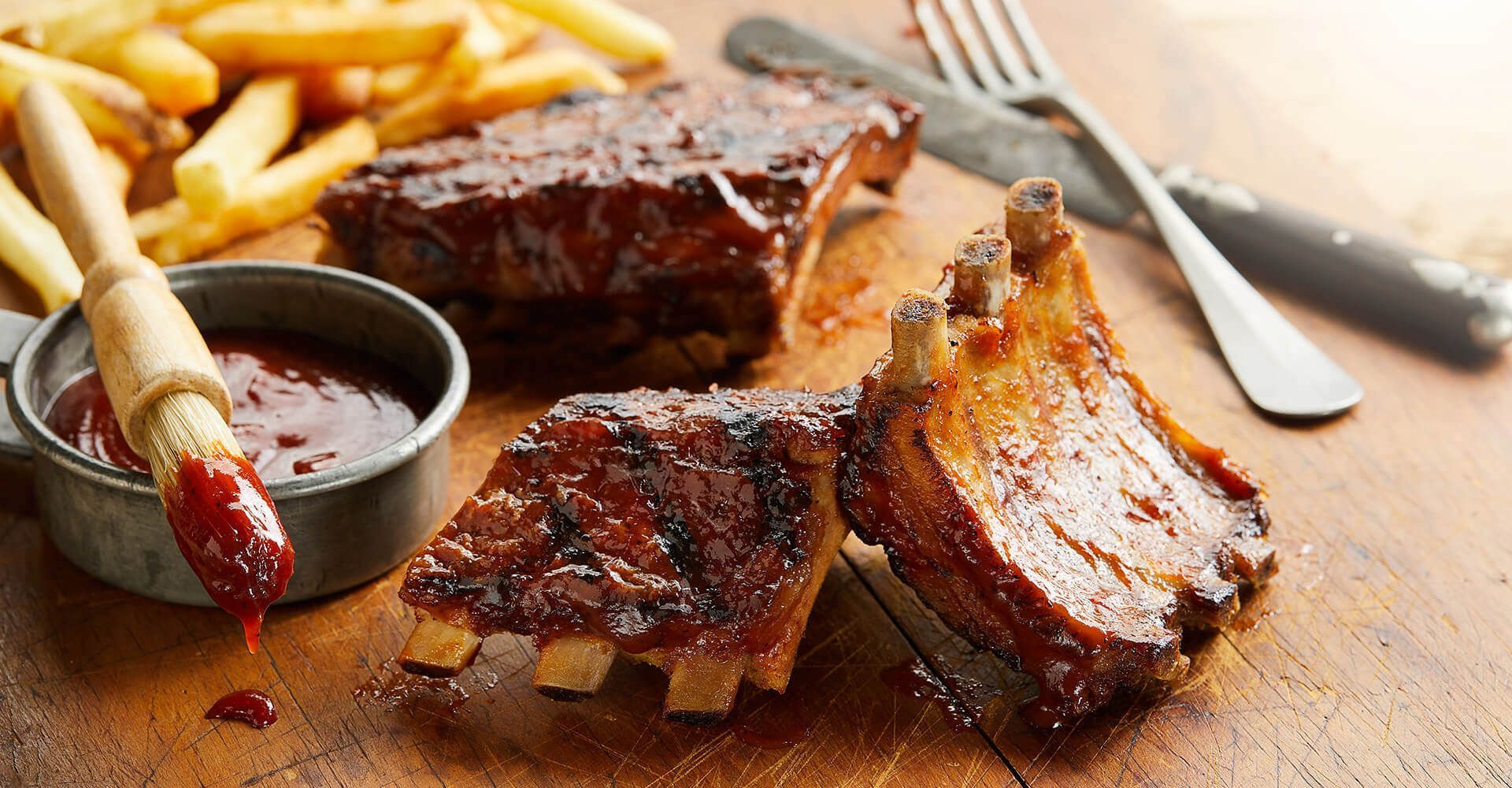 Ribs and french fries are on a wooden cutting board.