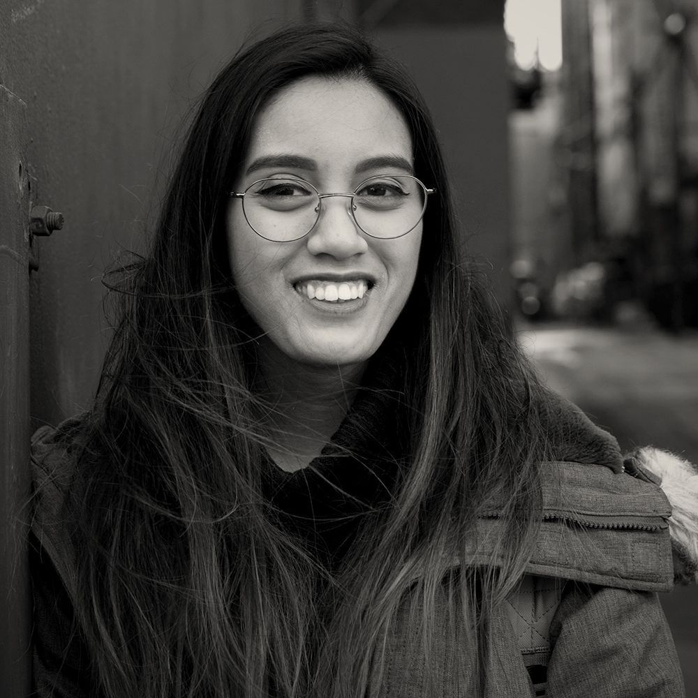 A woman wearing glasses and a jacket is smiling in a black and white photo.