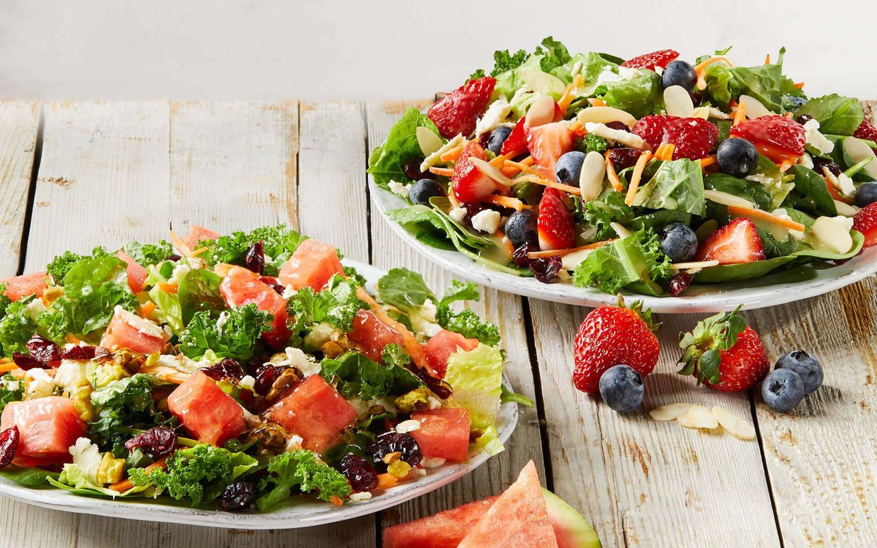 Two plates of salads with strawberries and blueberries on a wooden table.
