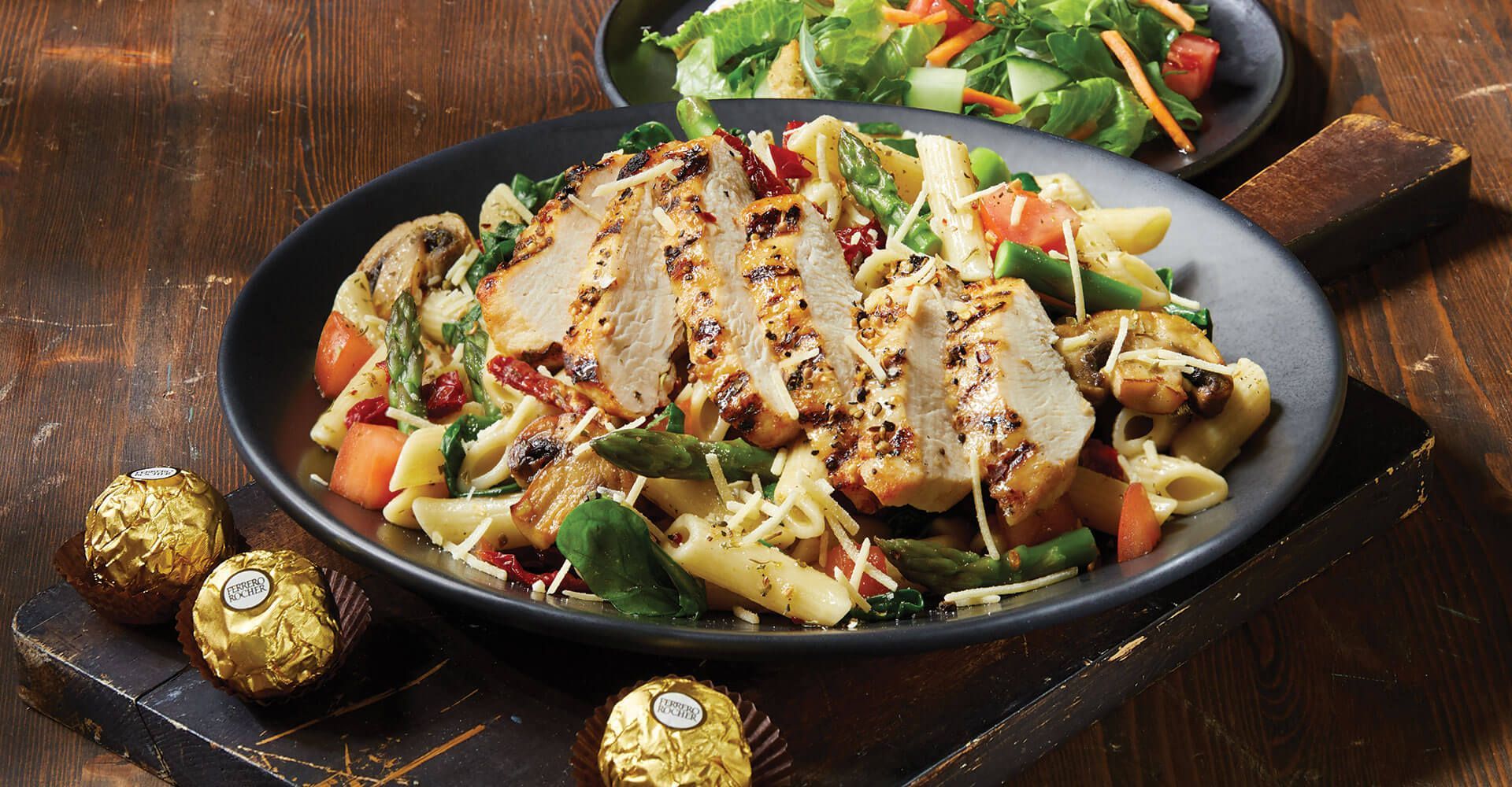 A plate of pasta with chicken and vegetables on a wooden table.