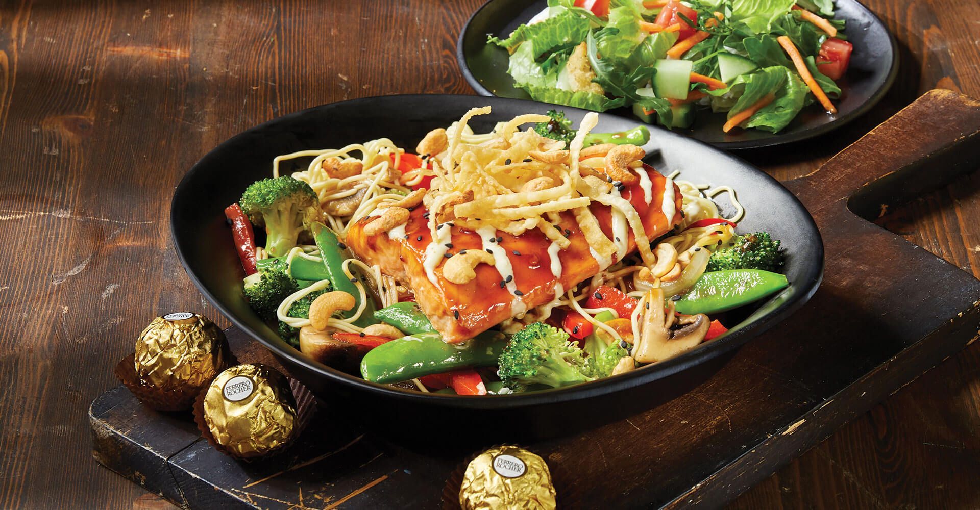 A plate of food with noodles and vegetables on a wooden table.