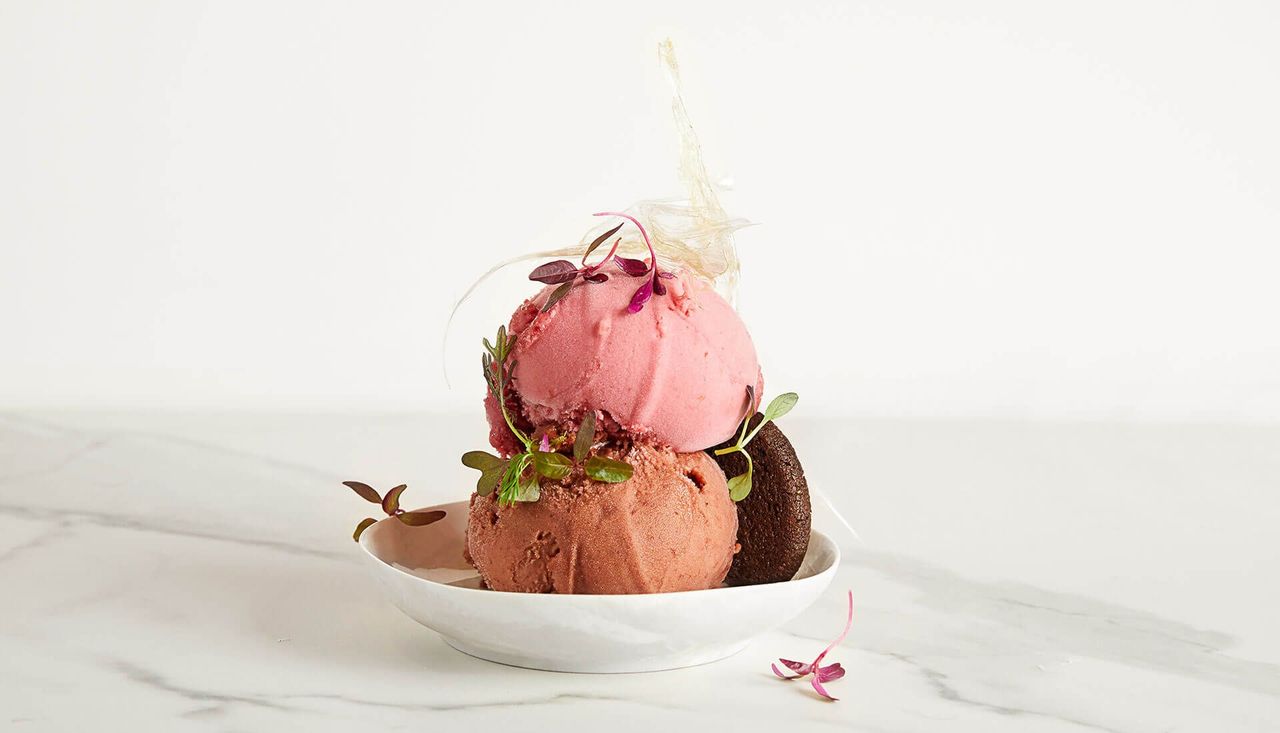 Two scoops of ice cream are stacked on top of each other on a white plate.