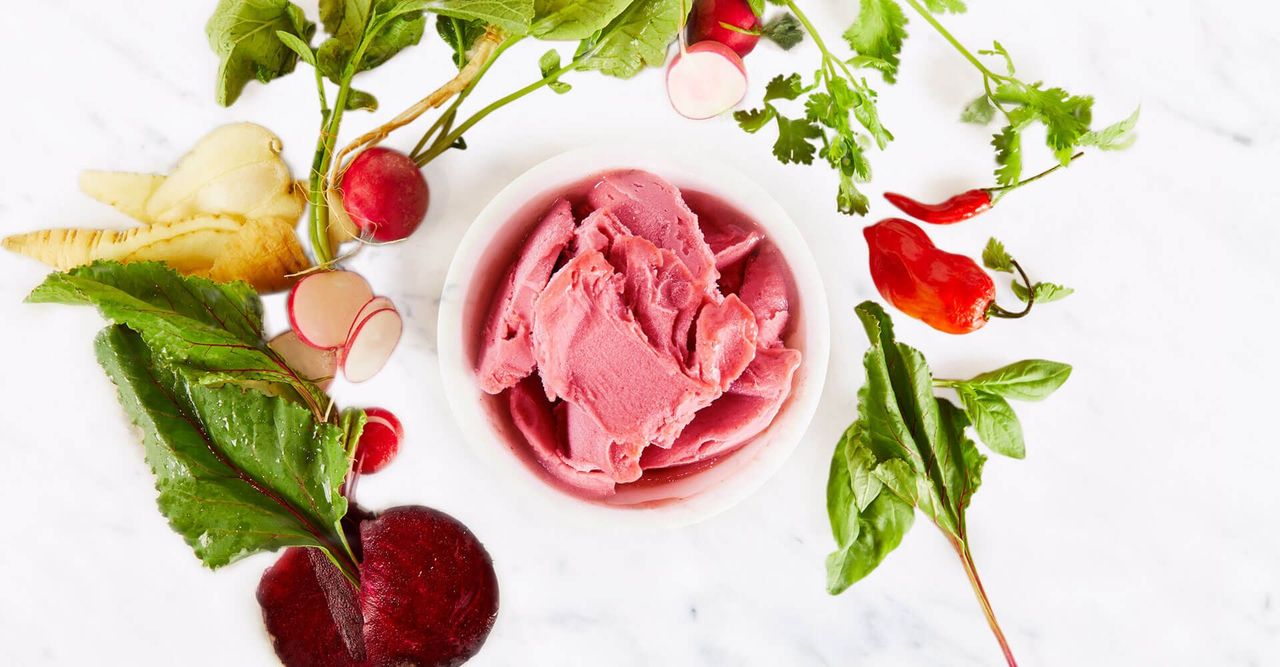 A bowl of ice cream surrounded by vegetables on a table.