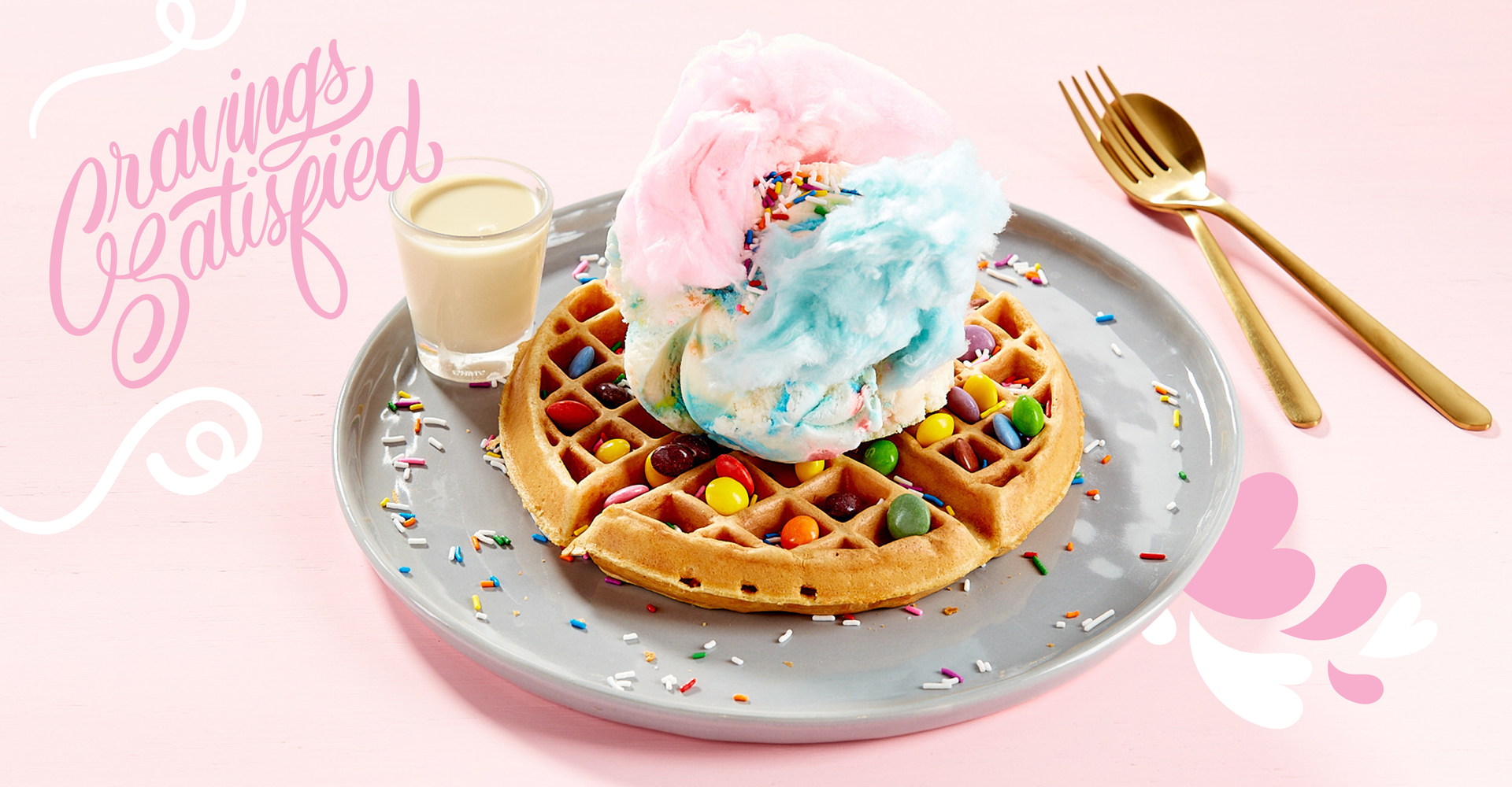 A waffle with cotton candy on top and a glass of milk on a plate.