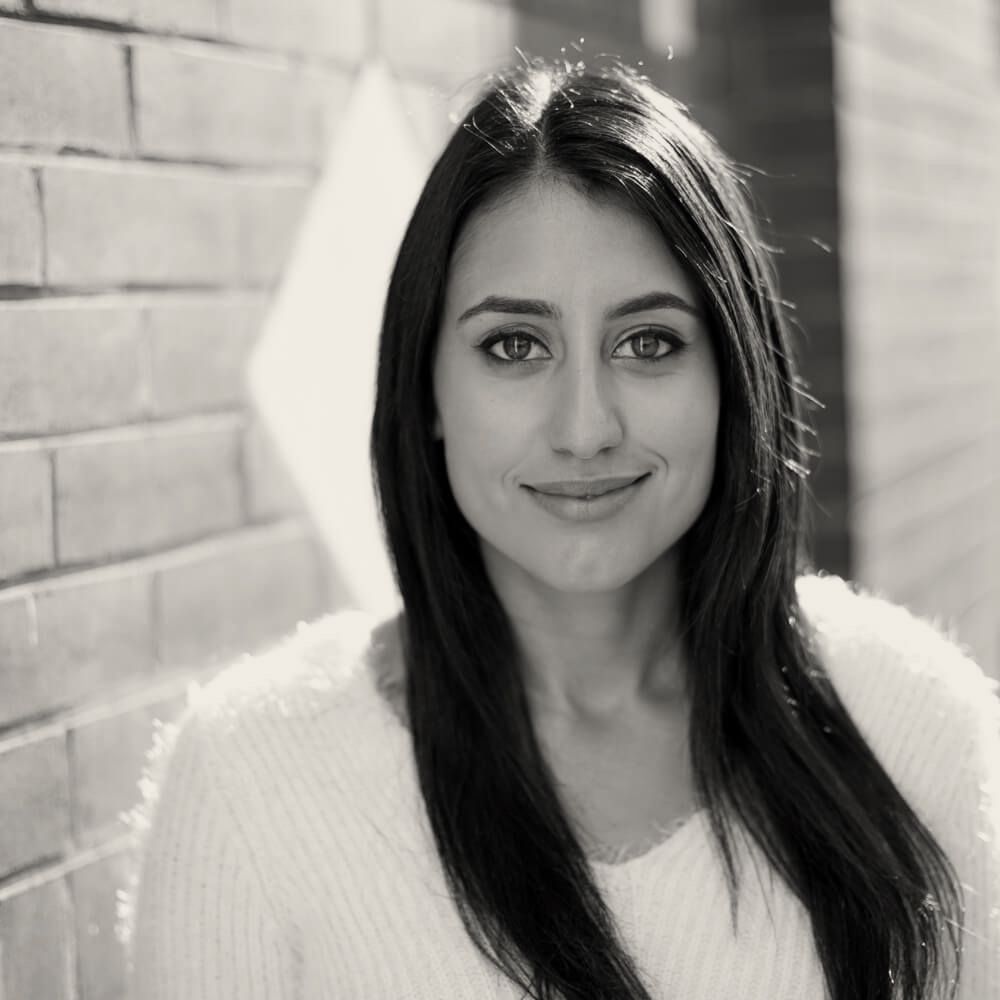 A black and white photo of a woman standing in front of a brick wall.