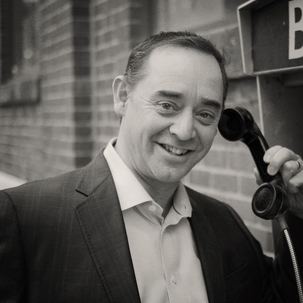 A man in a suit is talking on a pay phone.