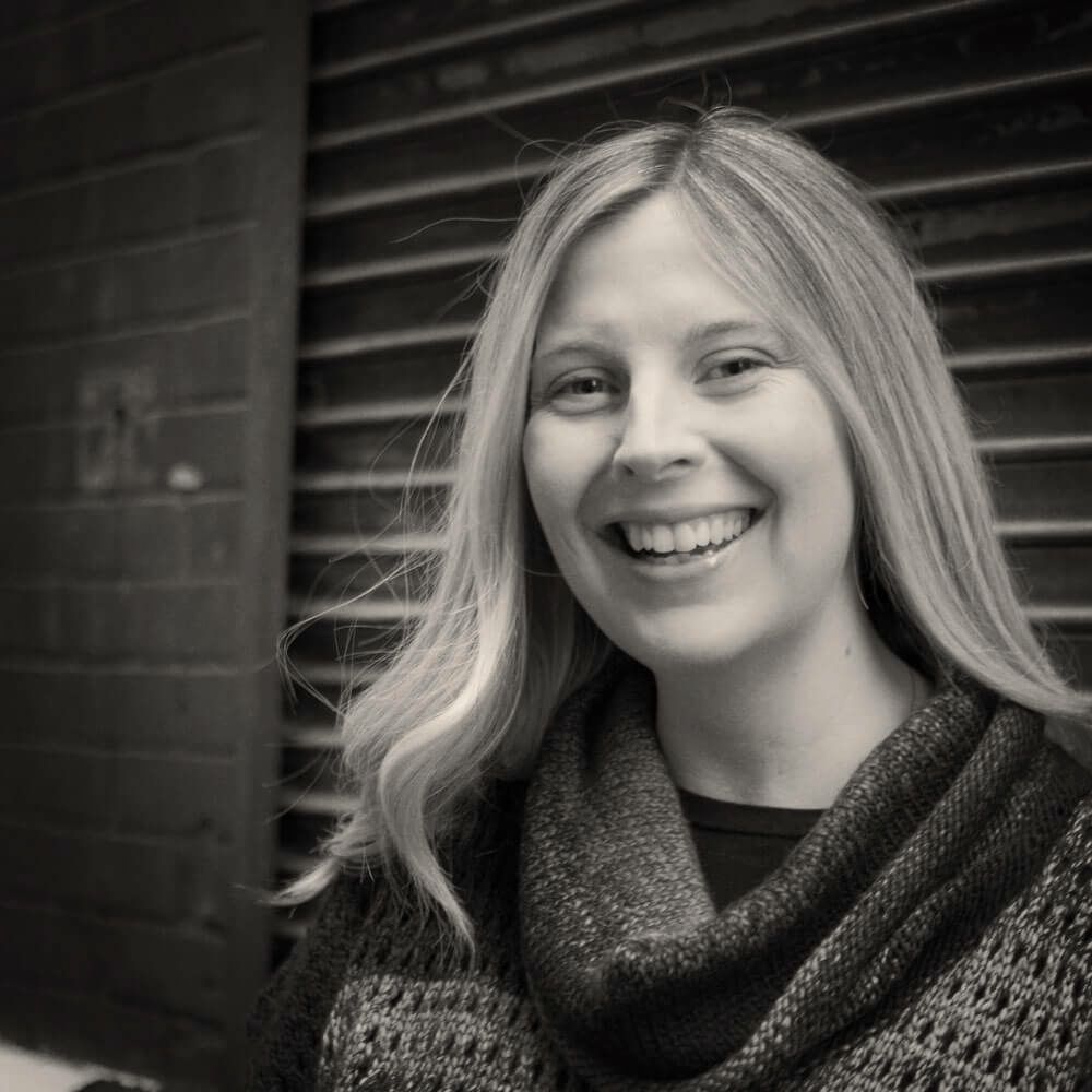A woman wearing a sweater and scarf is smiling in a black and white photo.