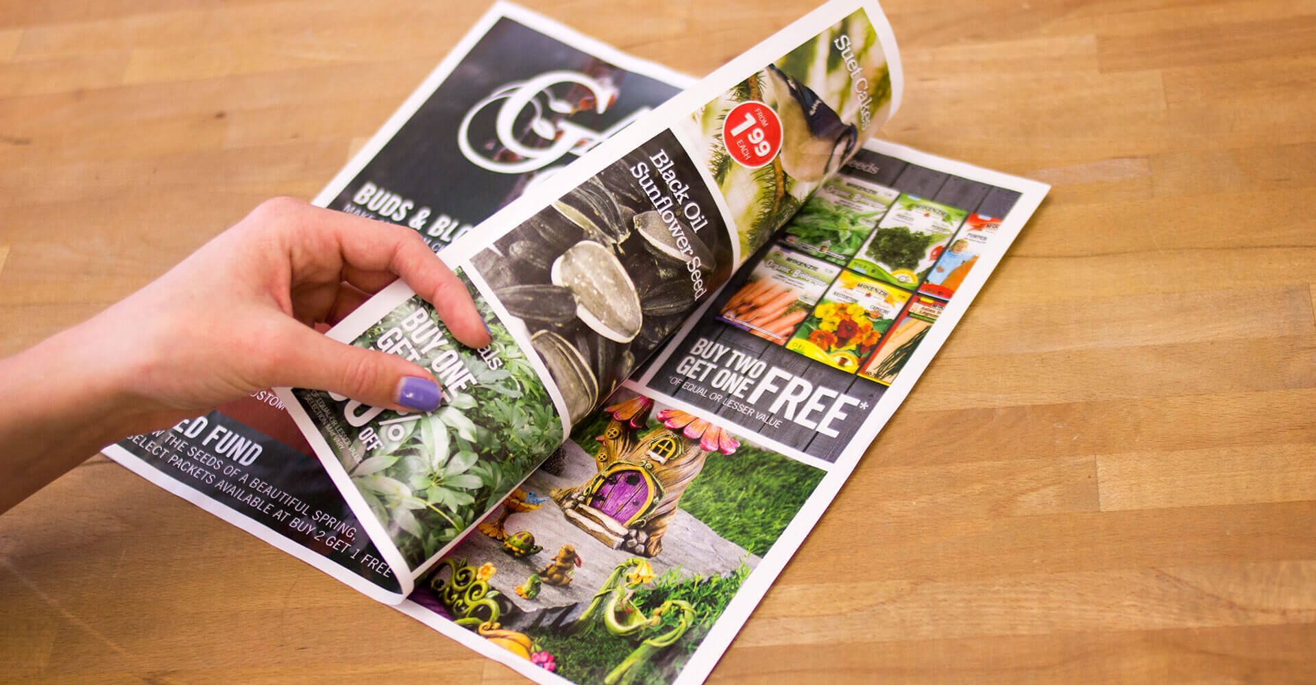 A person is opening a magazine on a wooden table.