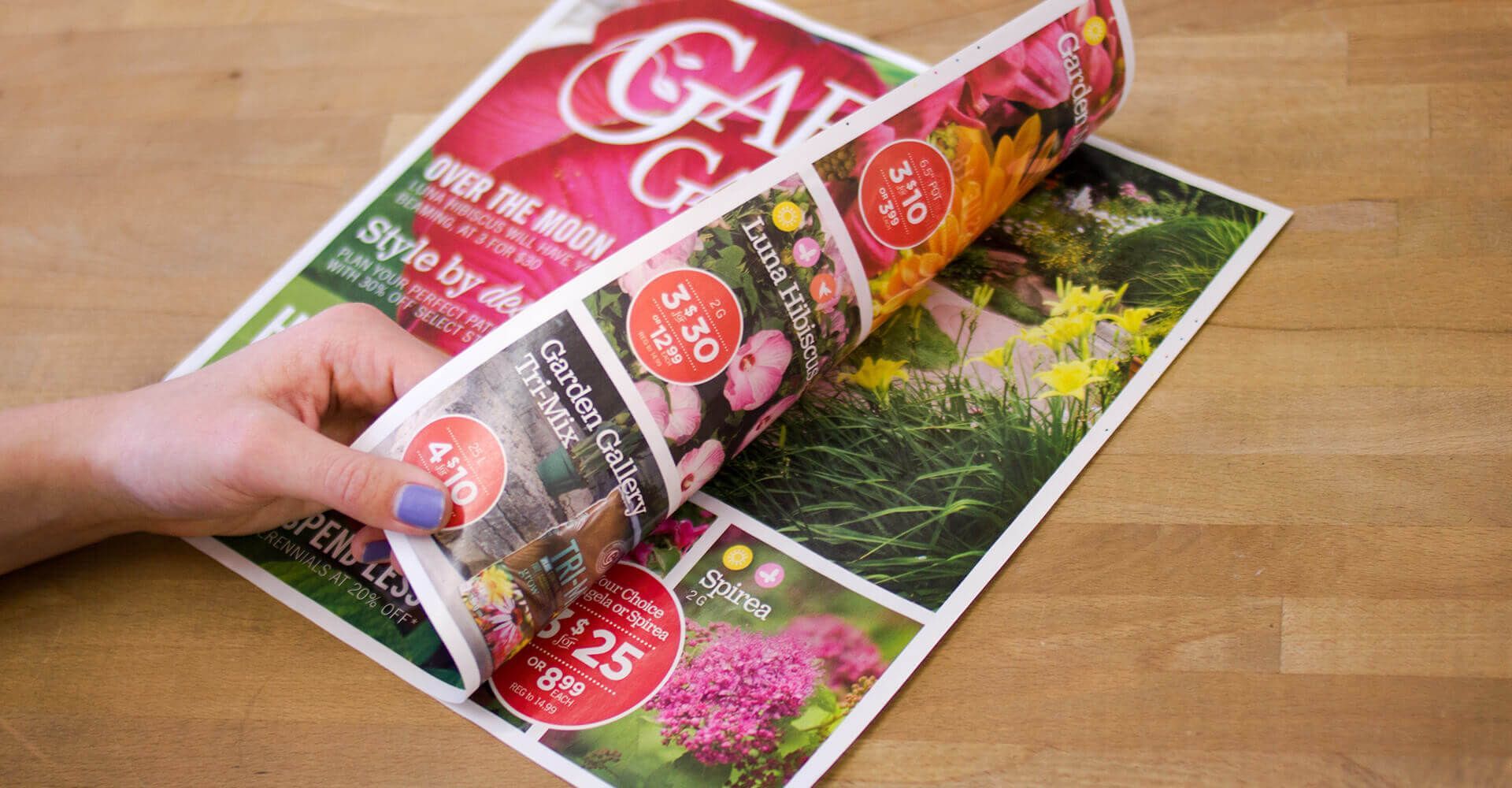A person is holding a magazine with flowers on it on a wooden table.
