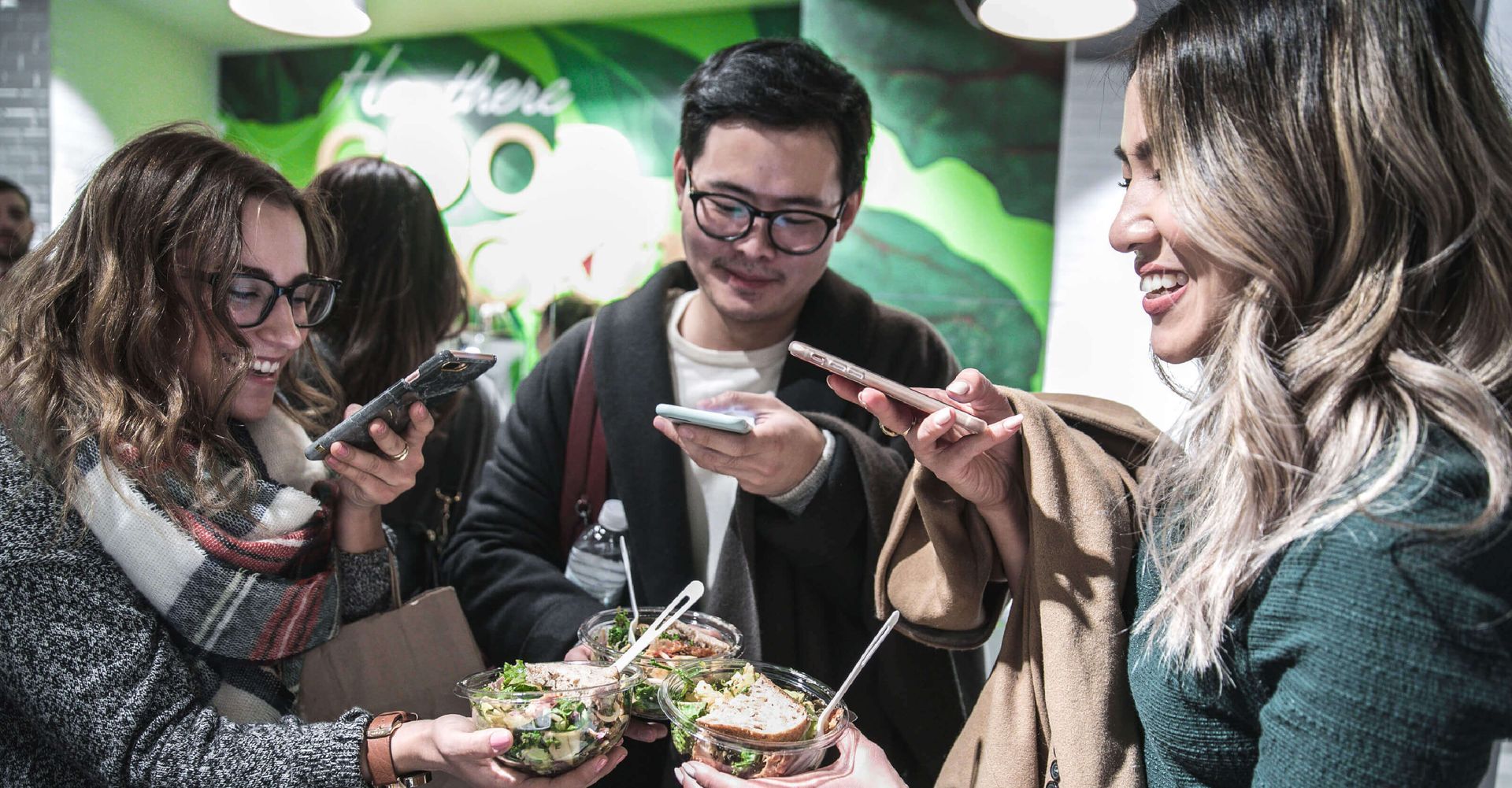 A group of people are holding sandwiches and looking at their phones.