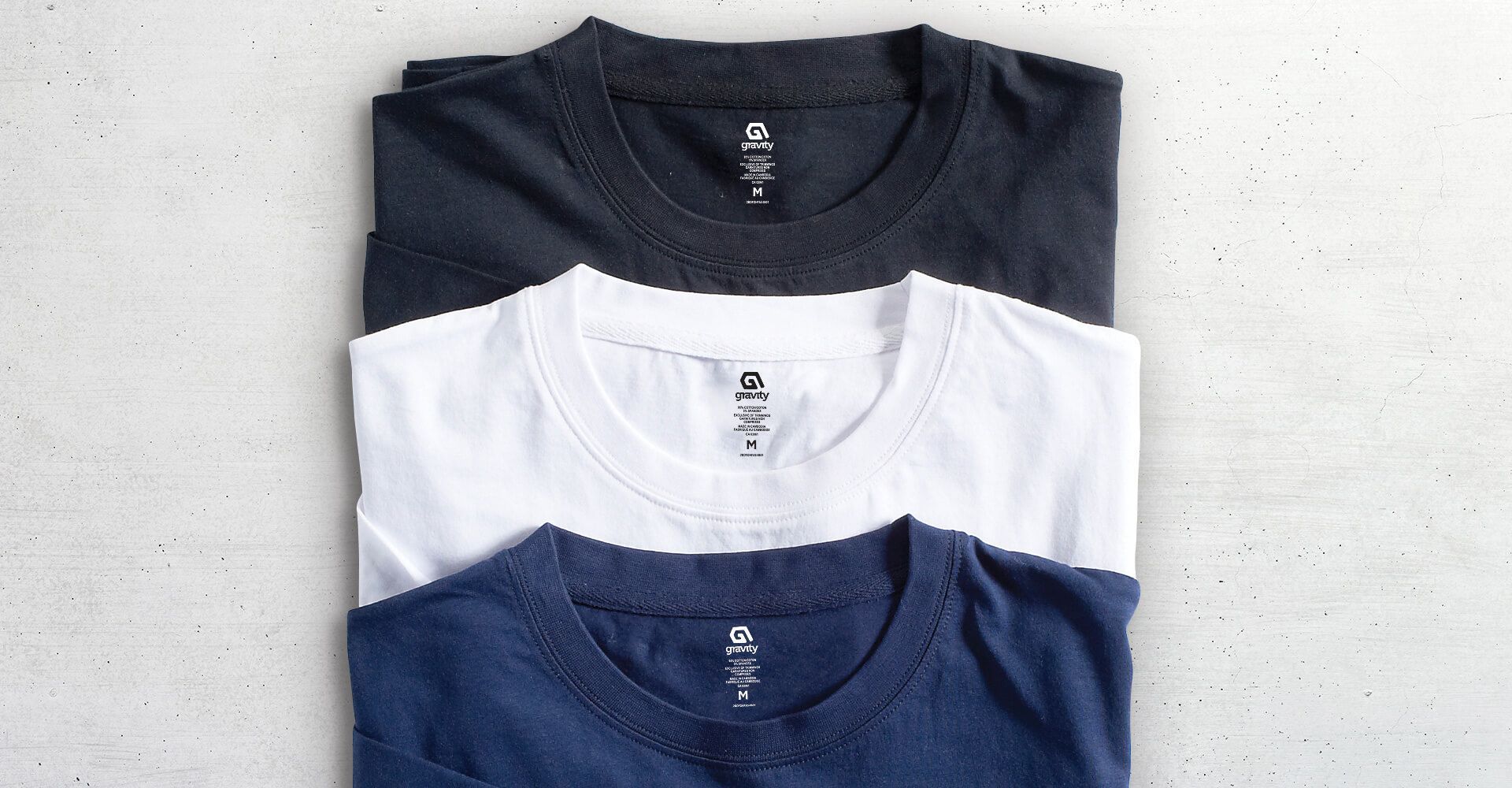 Three t-shirts are stacked on top of each other on a table.