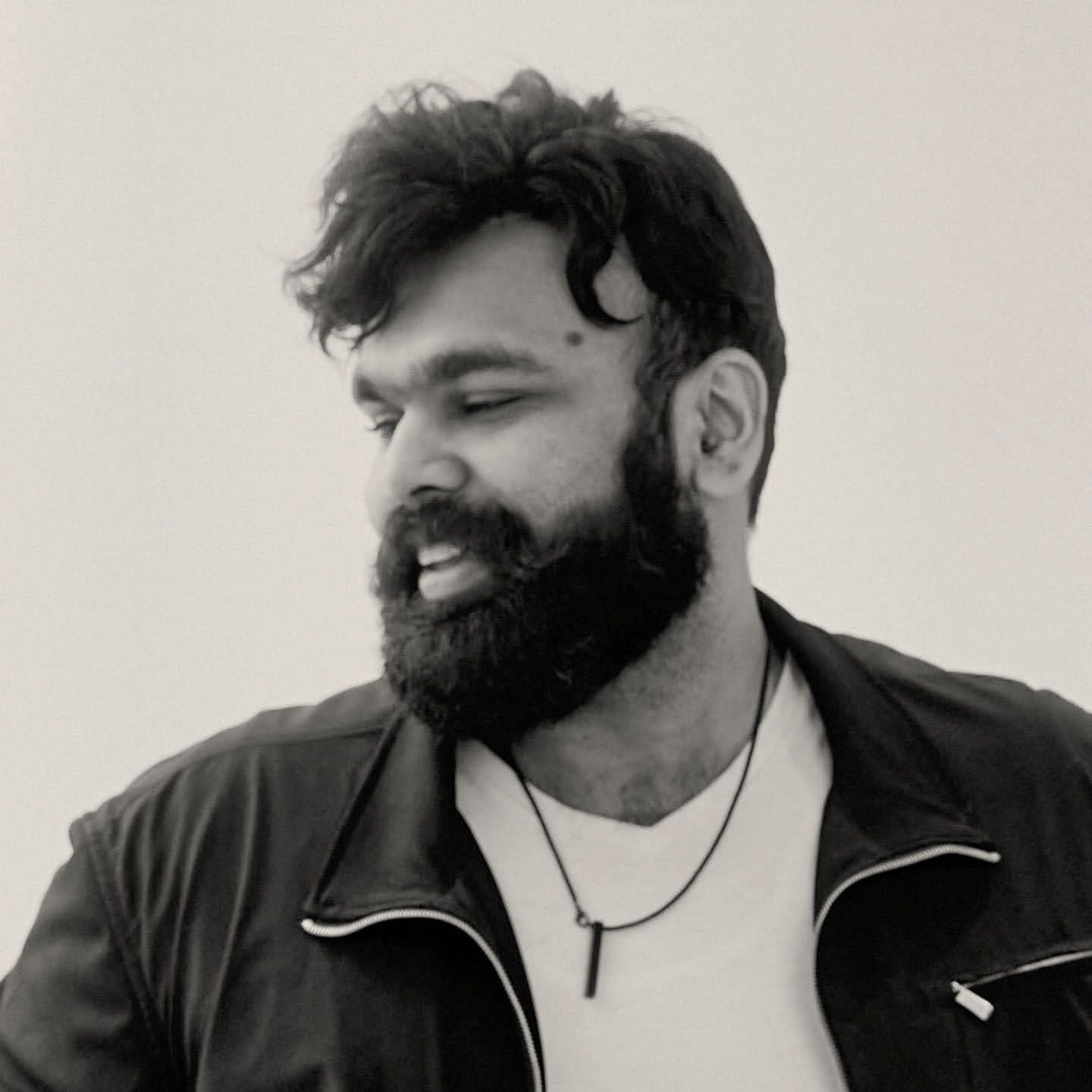 A man with a beard is wearing a white shirt and a black jacket.