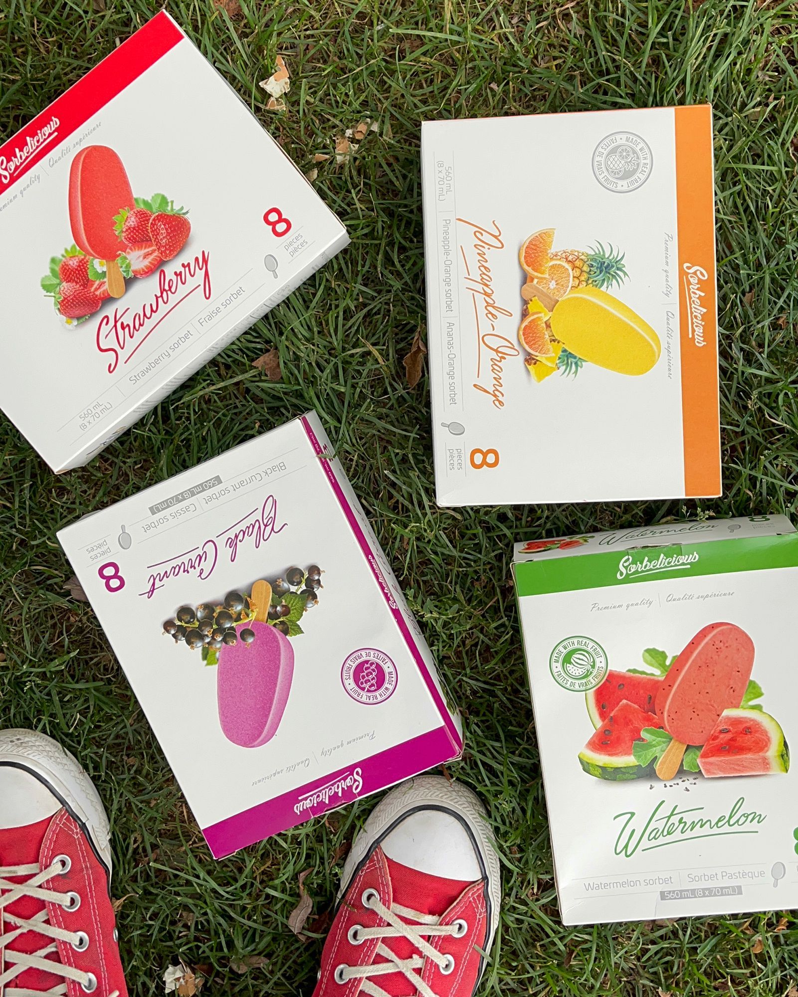 Four boxes of popsicles are sitting on top of a lush green field.