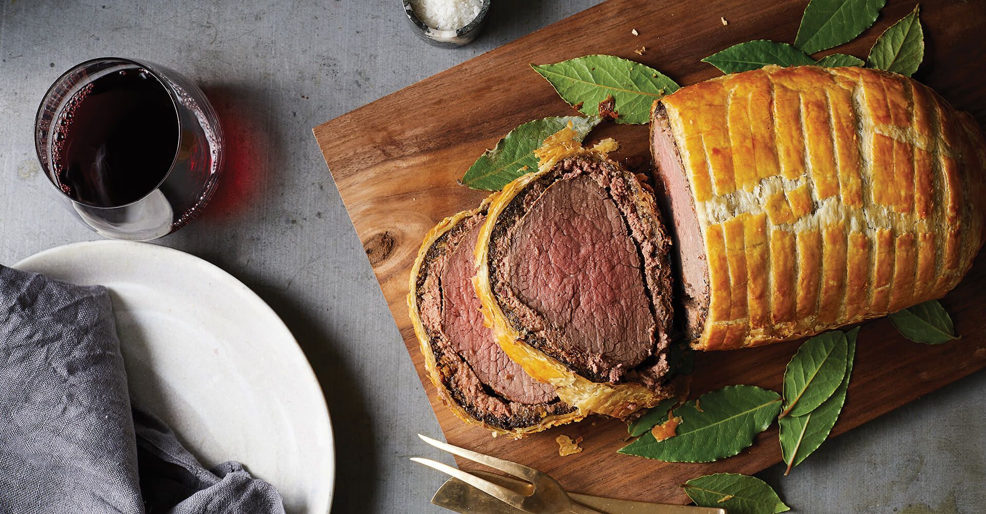 A piece of meat is sitting on a wooden cutting board next to a glass of wine.