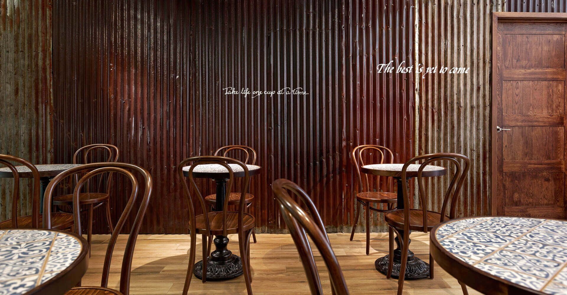 A row of tables and chairs in a restaurant with a corrugated metal wall.