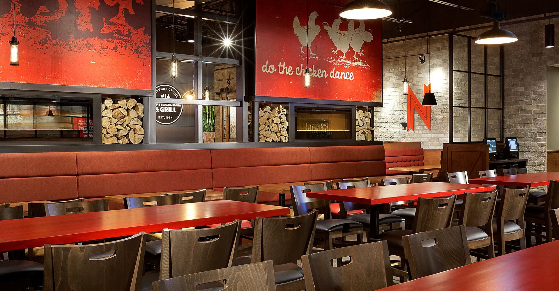 A restaurant with red tables and chairs and a chicken on the wall