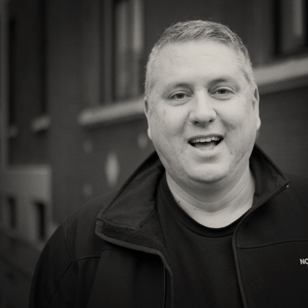 A man in a black jacket is smiling in a black and white photo.