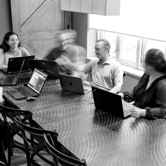 A group of people are sitting around a table with laptops.