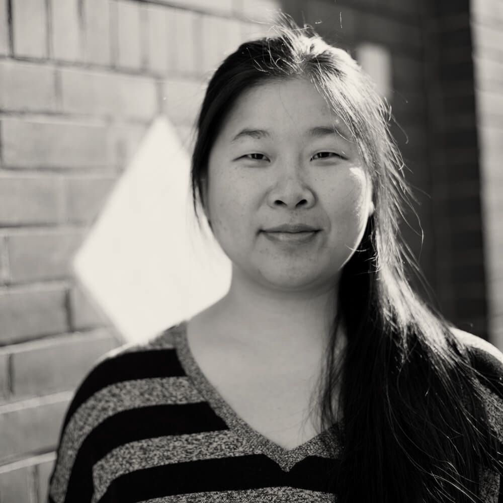 A black and white photo of a woman standing in front of a brick wall.