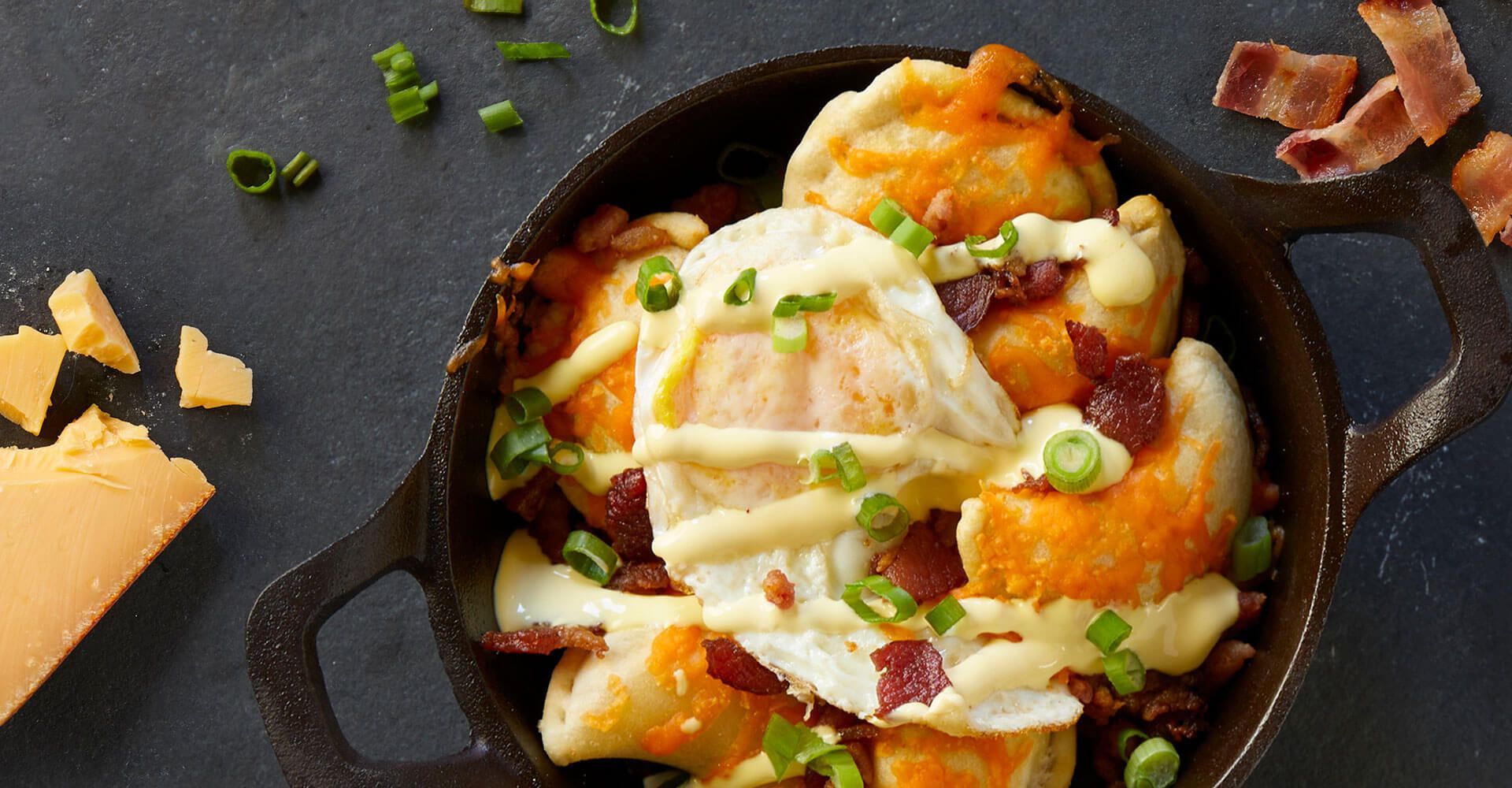 A skillet filled with potatoes , eggs , bacon and cheese.