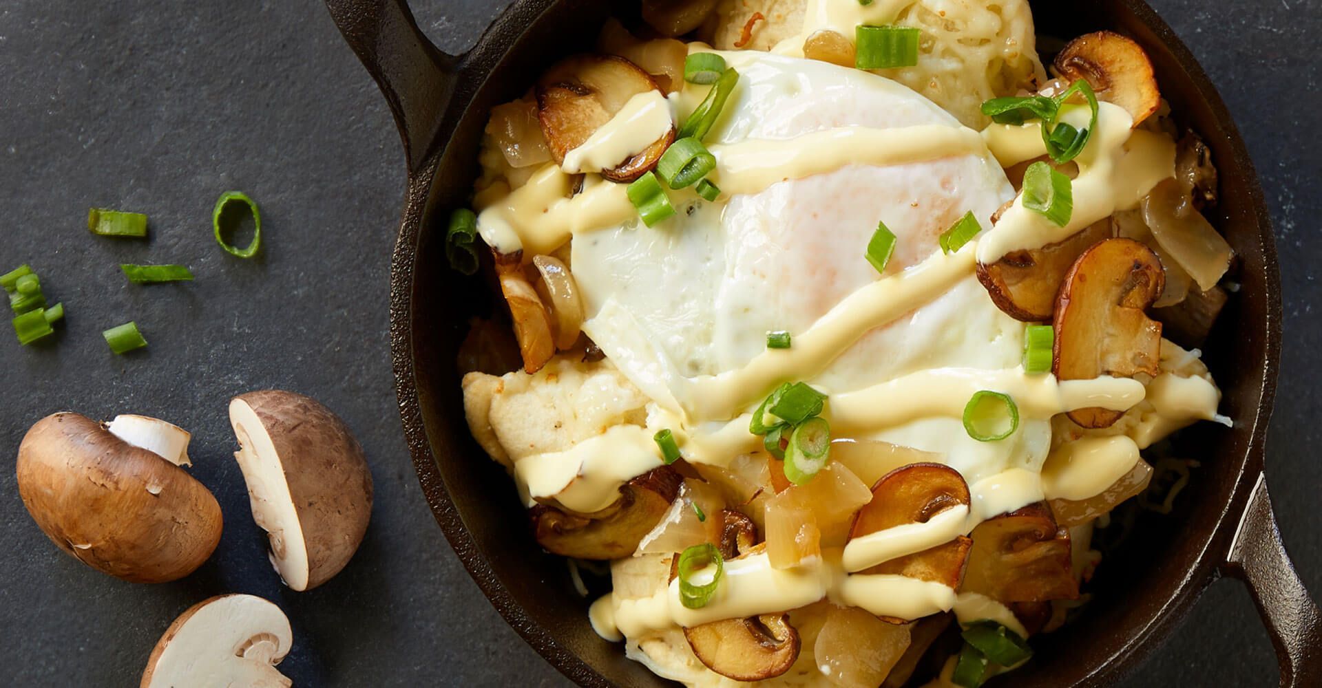 A skillet filled with potatoes , mushrooms , and a fried egg.