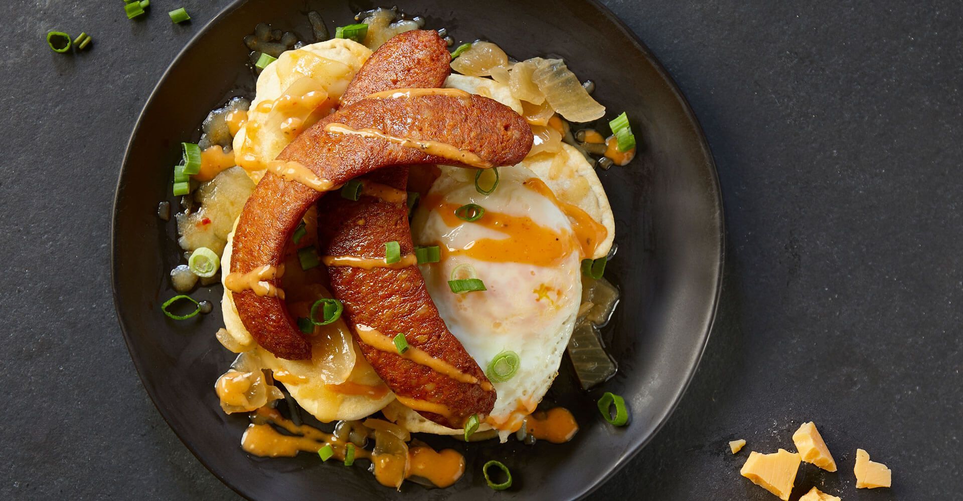 A black plate topped with mashed potatoes , eggs , bacon and cheese.