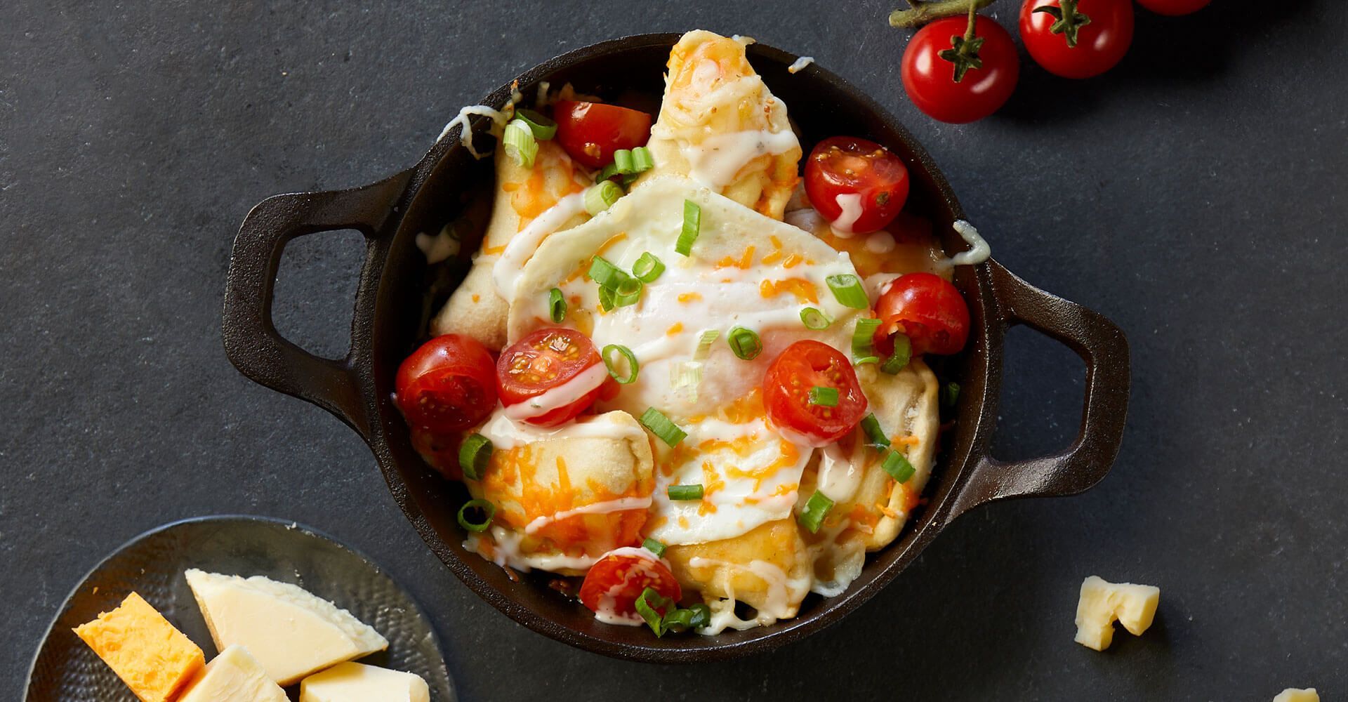 A skillet filled with food and tomatoes on a table.