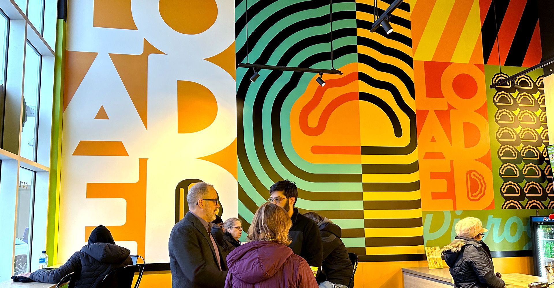 A group of people are standing in front of a colorful wall in a restaurant.