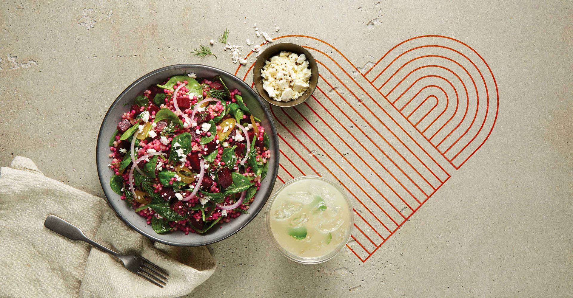 A bowl of salad is sitting on a table next to a heart drawn on the floor.