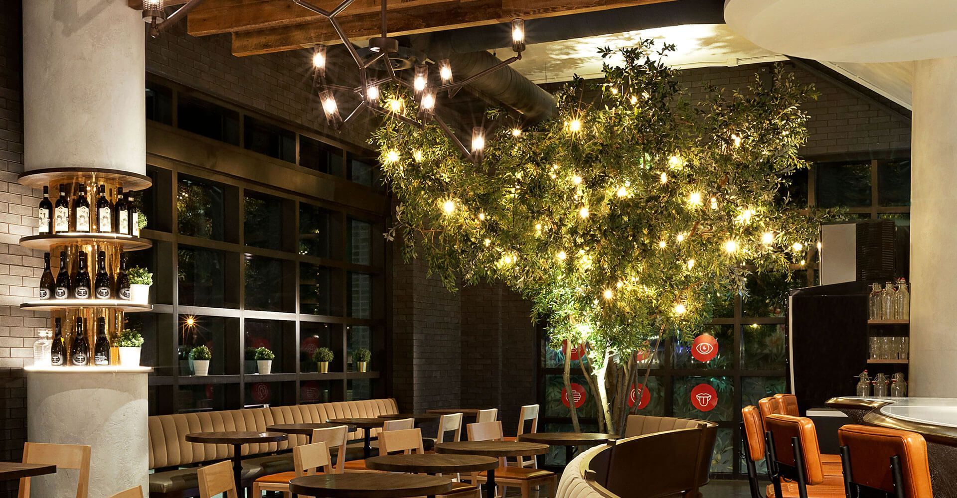 A restaurant with tables and chairs and a tree in the middle of the room.