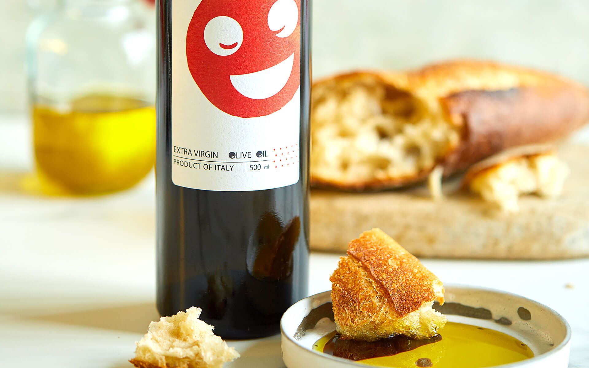 A bottle of olive oil next to a bowl of bread and a loaf of bread on a table.