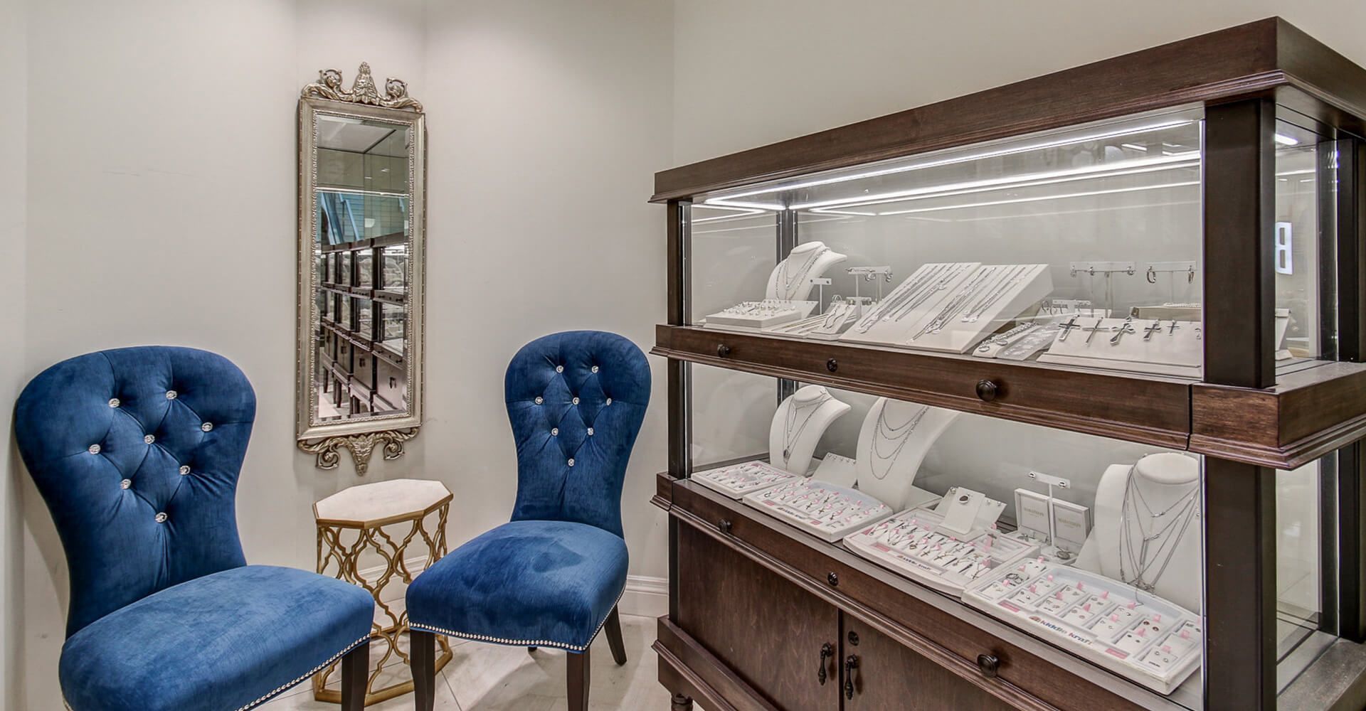 A room with two chairs and a display case filled with jewelry.