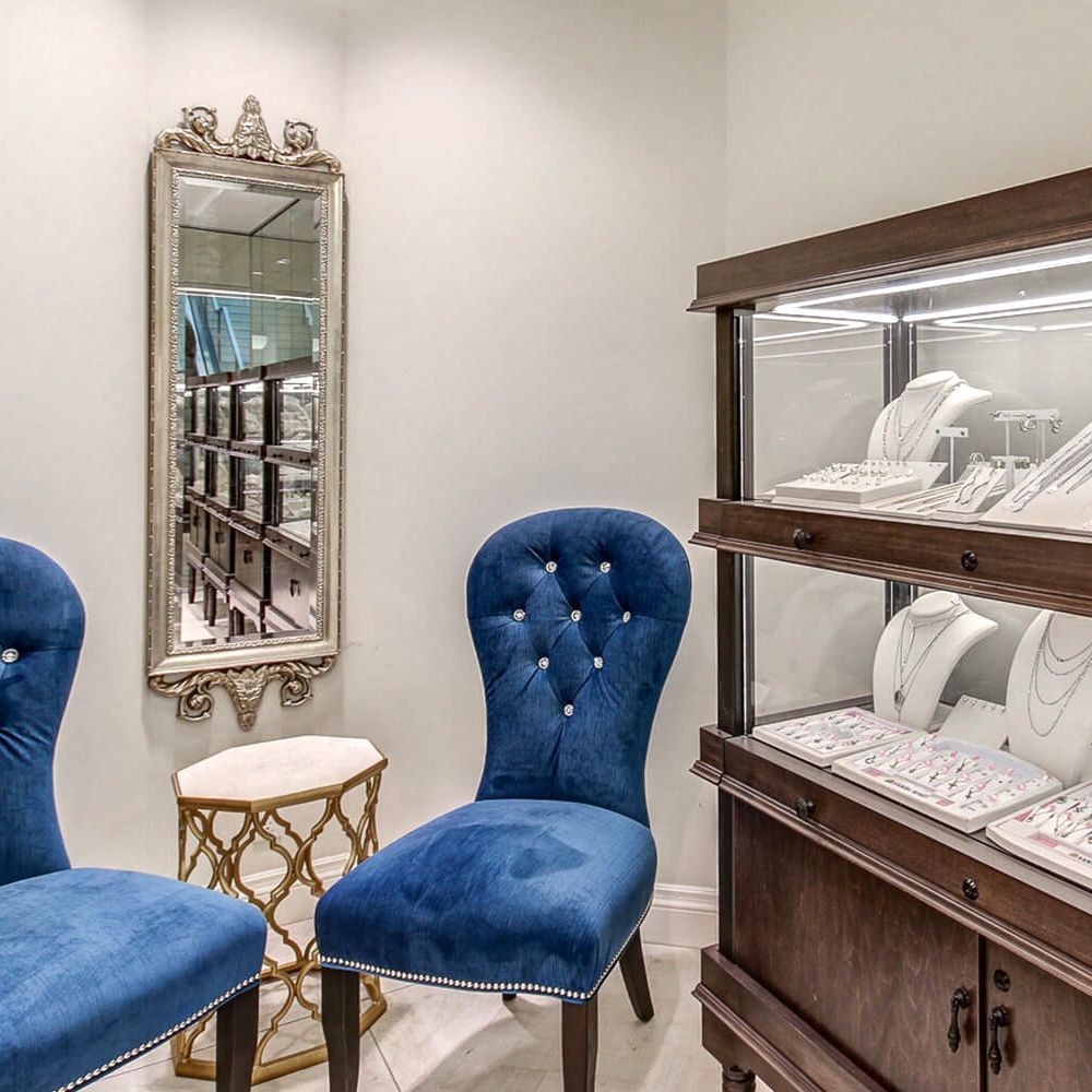A room with two blue chairs and a display case with necklaces on it.
