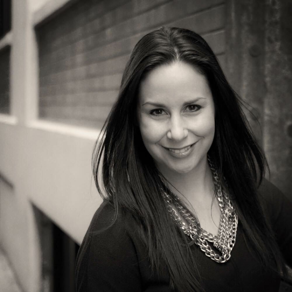 A black and white photo of a woman wearing a necklace and smiling.