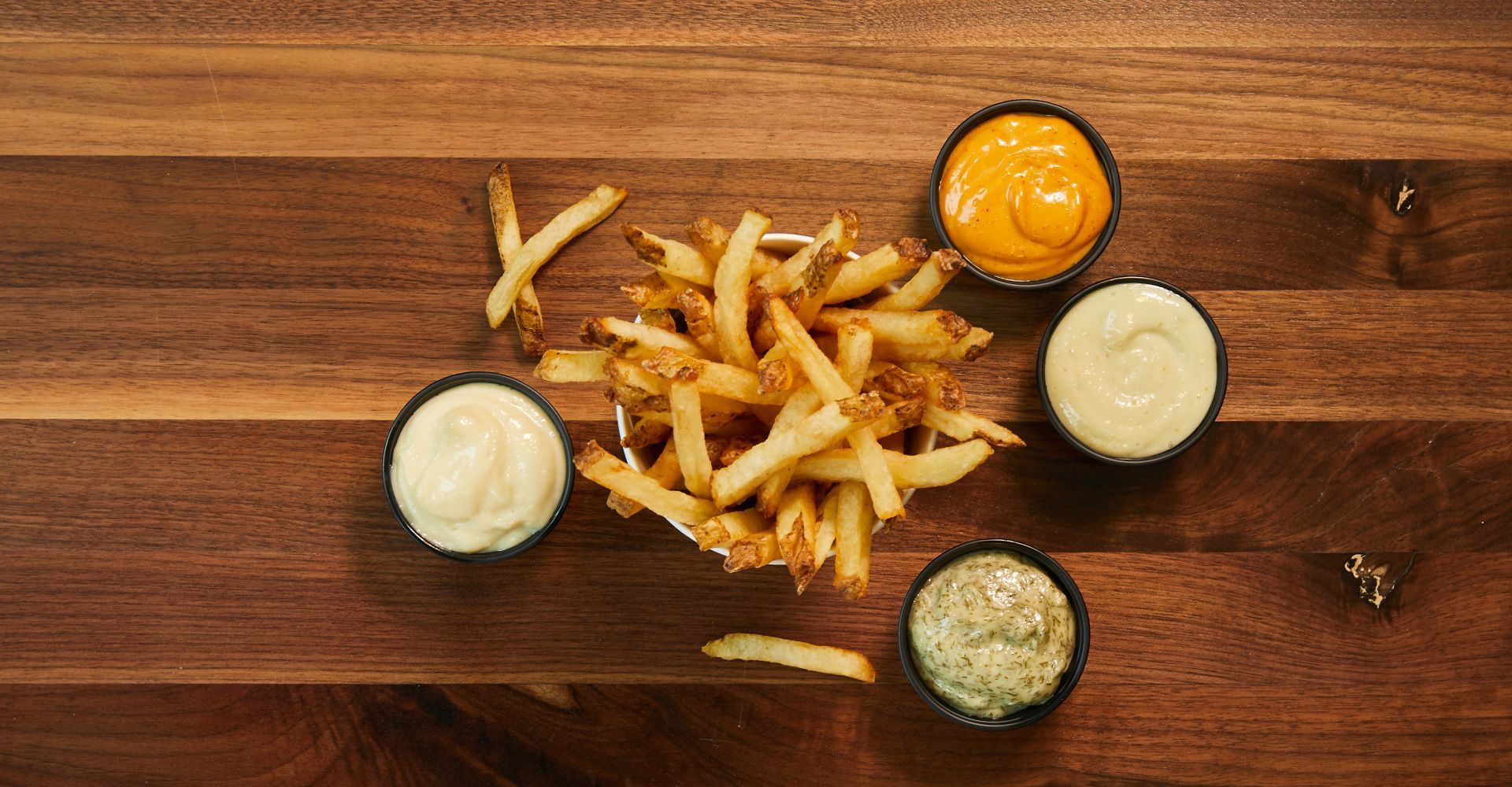 A wooden table topped with french fries and dipping sauces.