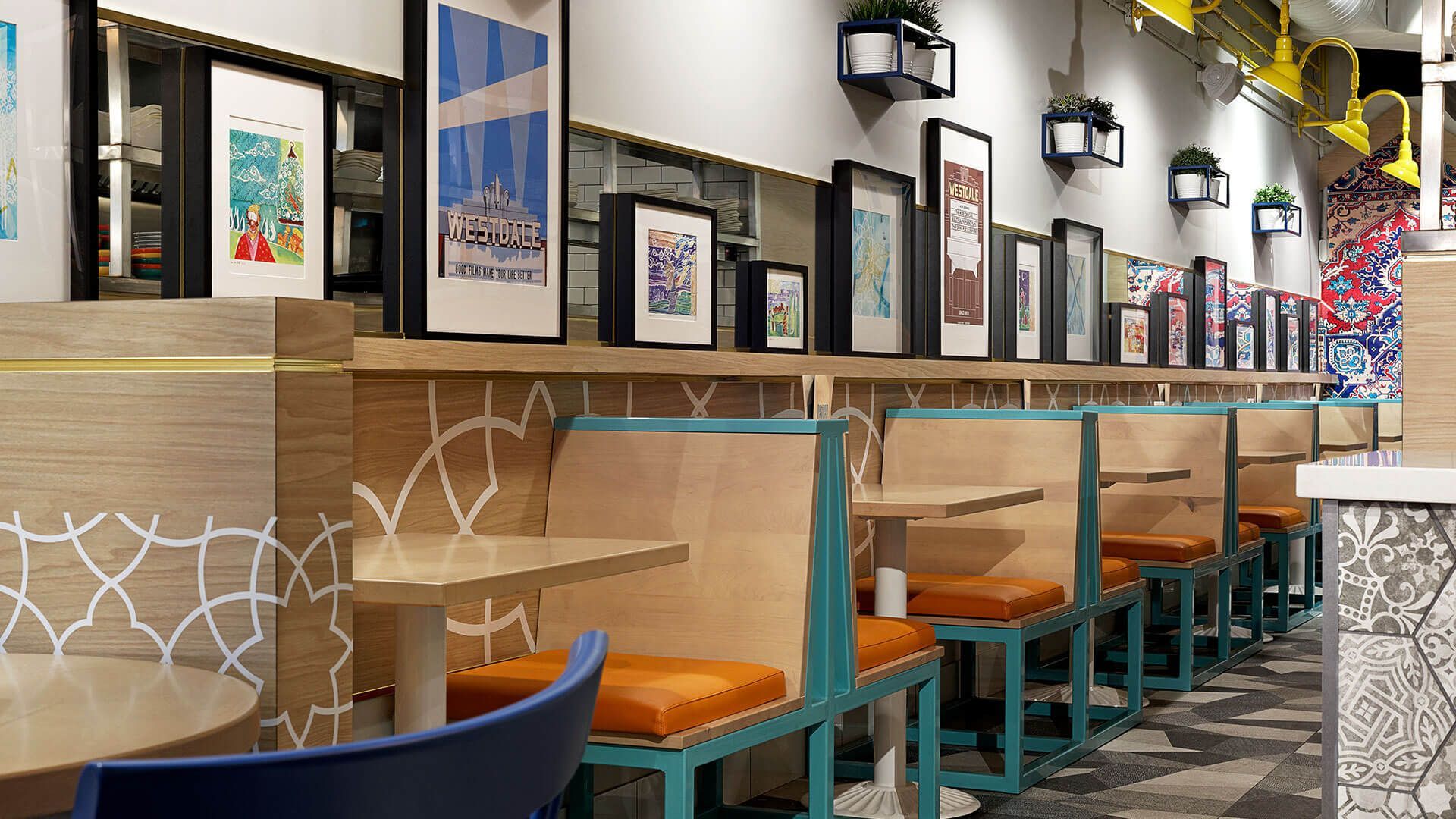 A row of tables and benches in a restaurant with pictures on the wall.