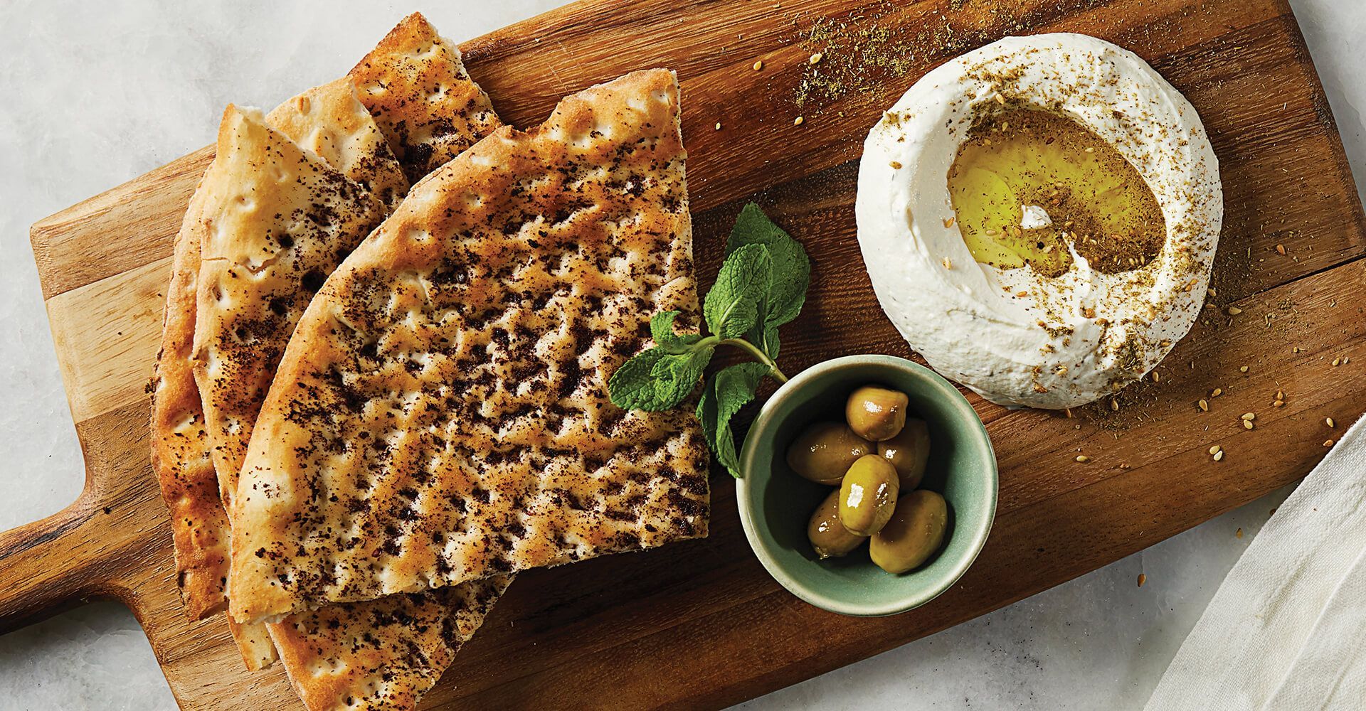 A wooden cutting board topped with bread , hummus and olives.