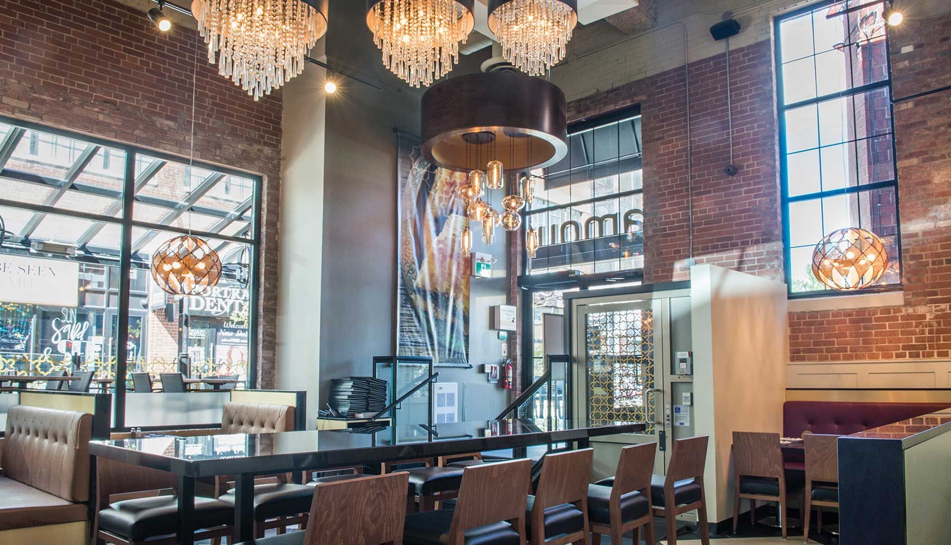 A restaurant with a long table and chairs and chandeliers hanging from the ceiling.