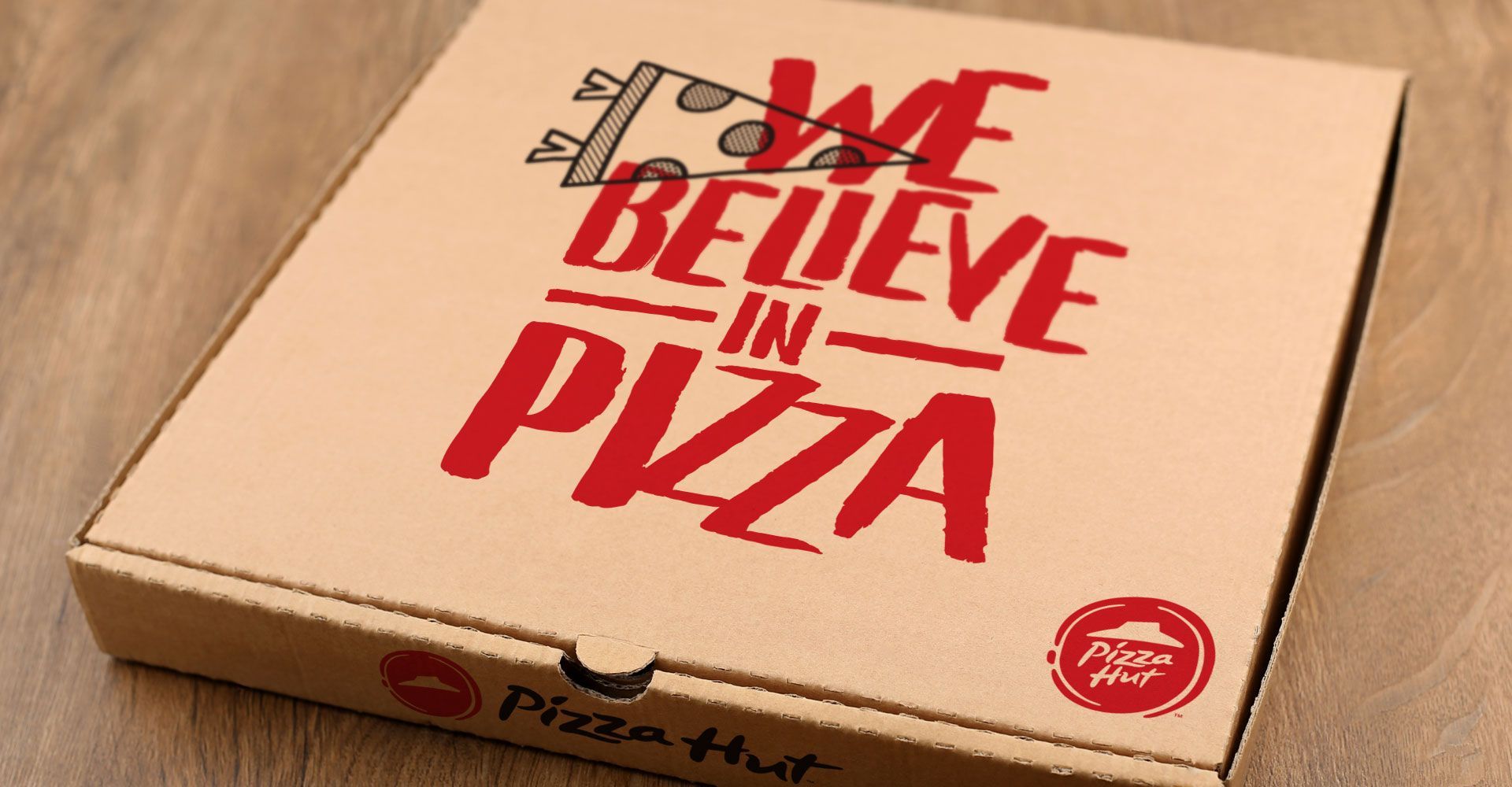 A pizza box that says `` we believe in pizza '' is sitting on a wooden table.