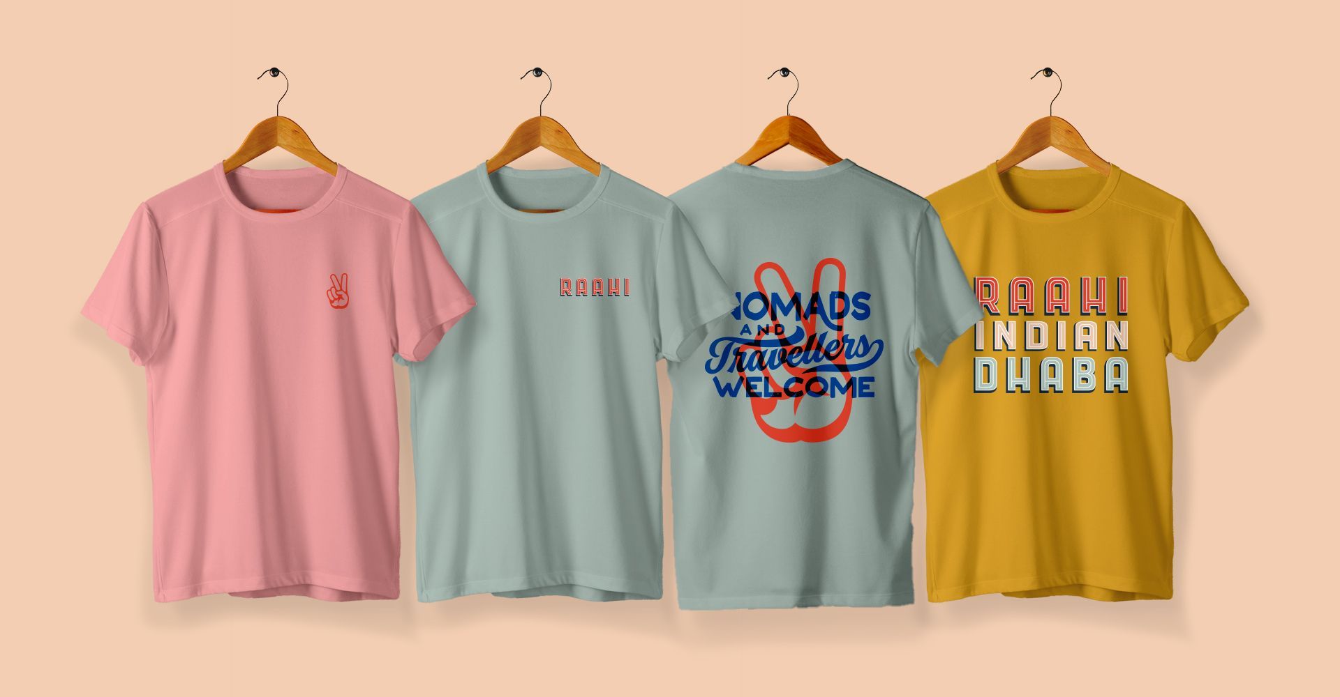 Three t-shirts are hanging on wooden hangers on a wall.