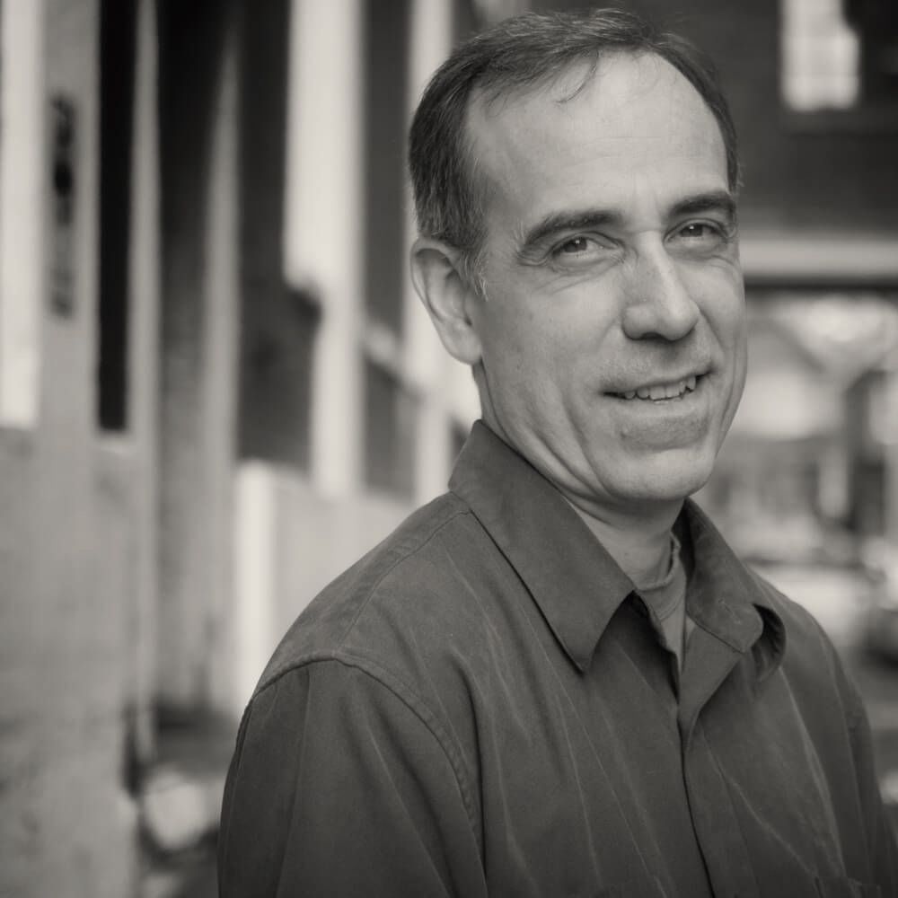 A man in a blue shirt is smiling in a black and white photo.