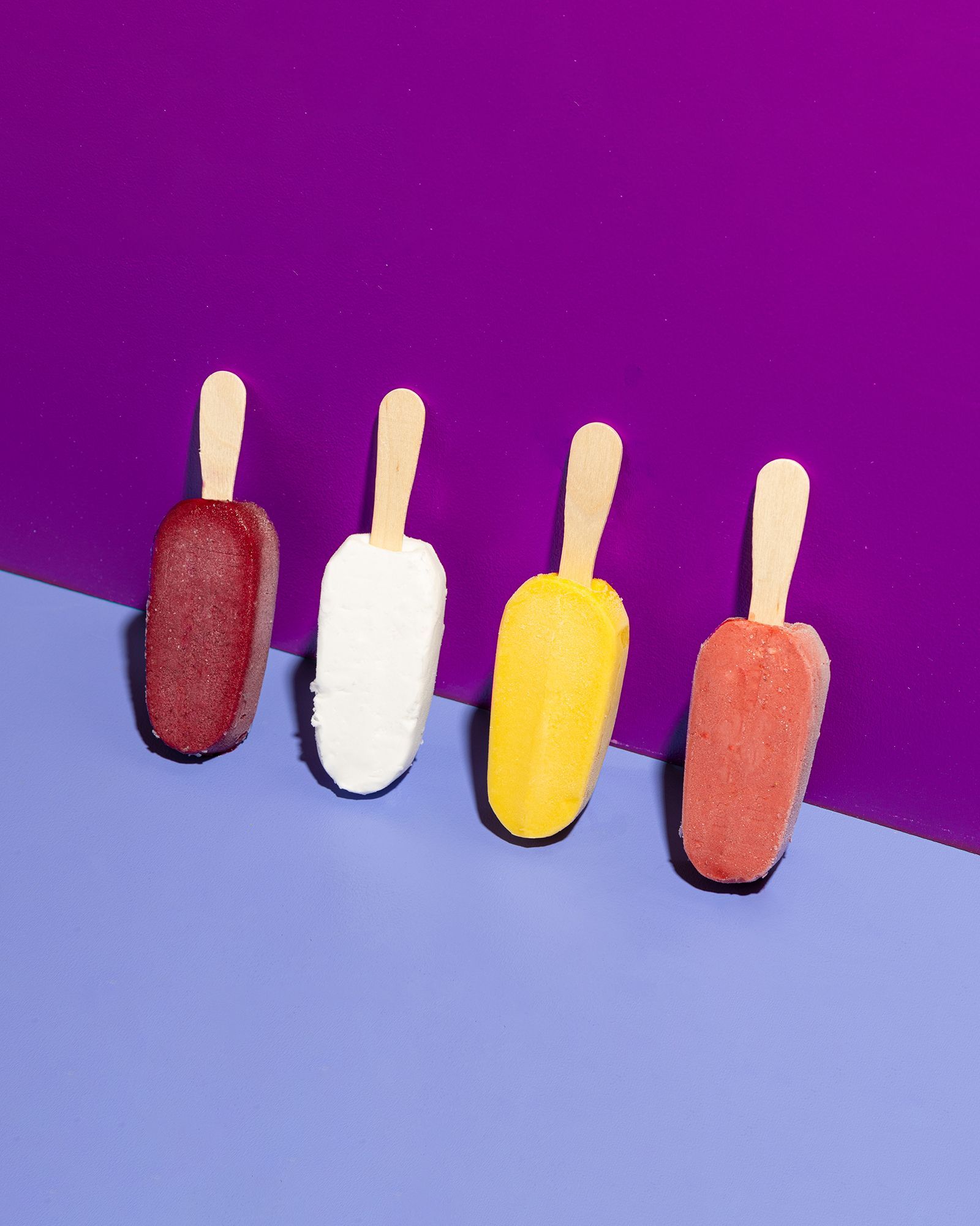Four different flavors of ice cream on sticks on a purple and blue surface.