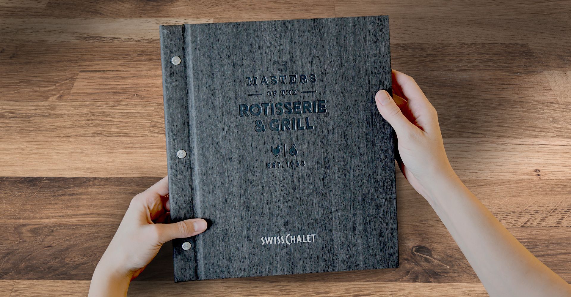 A person is holding a menu in their hands on a wooden table.