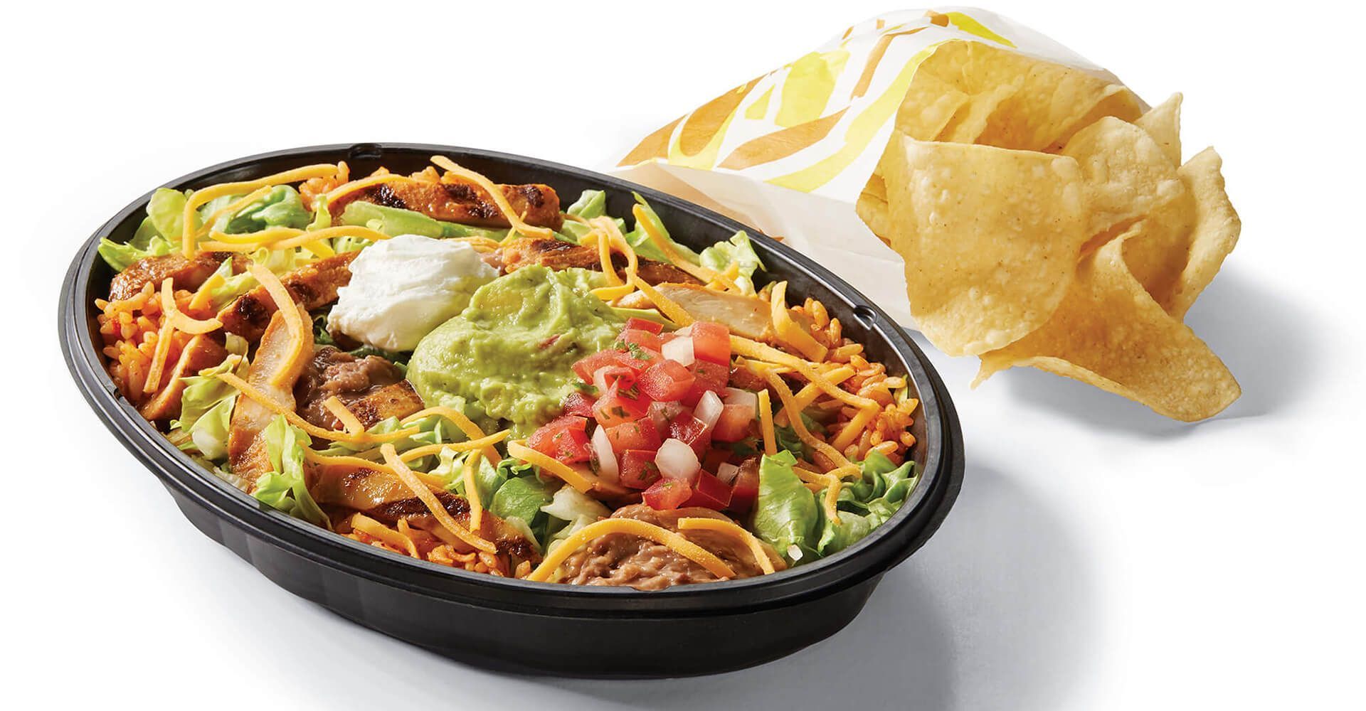 A bowl of mexican food next to a bag of tortilla chips.
