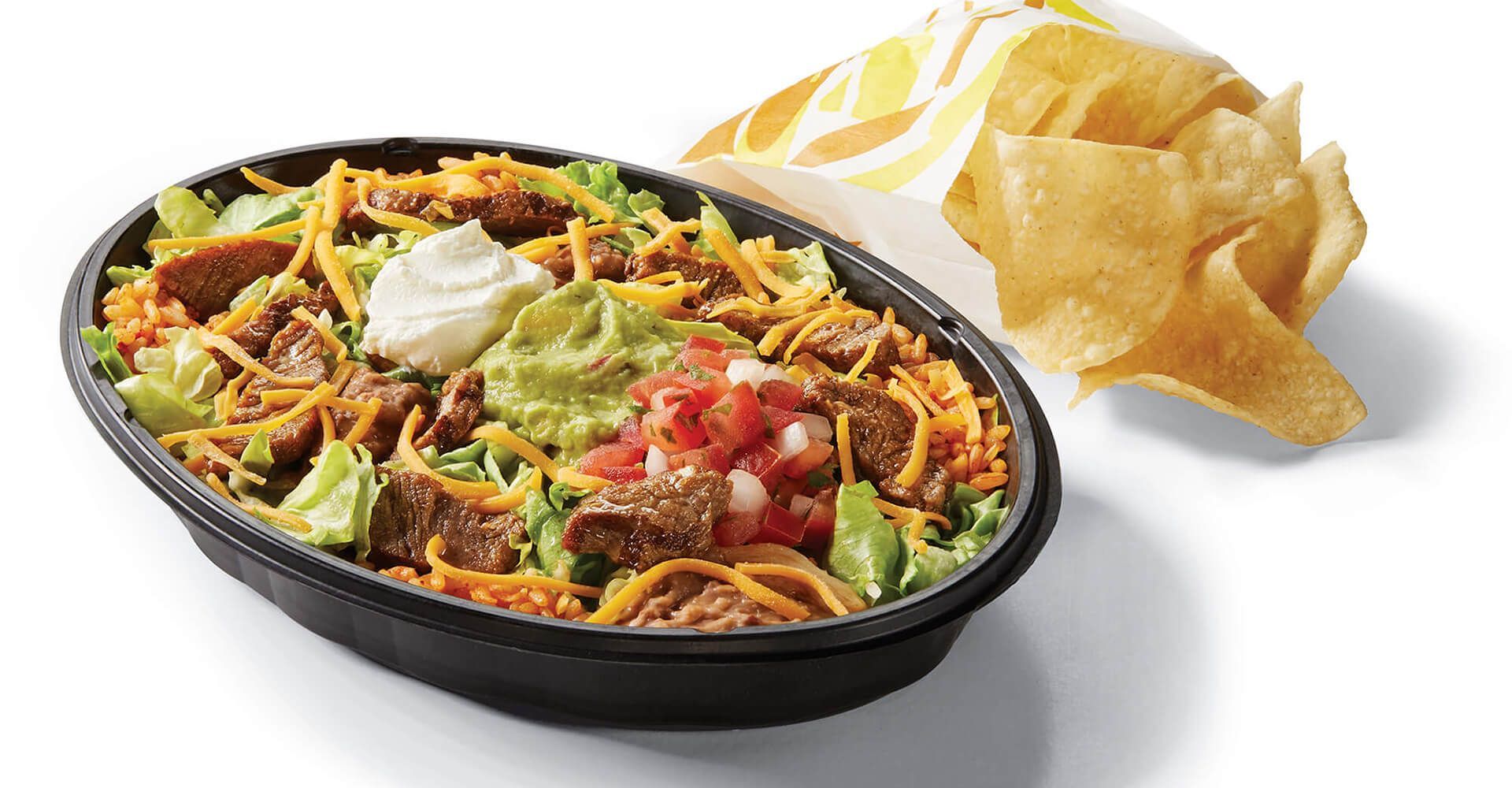 A bowl of food with guacamole and sour cream next to a bowl of tortilla chips.